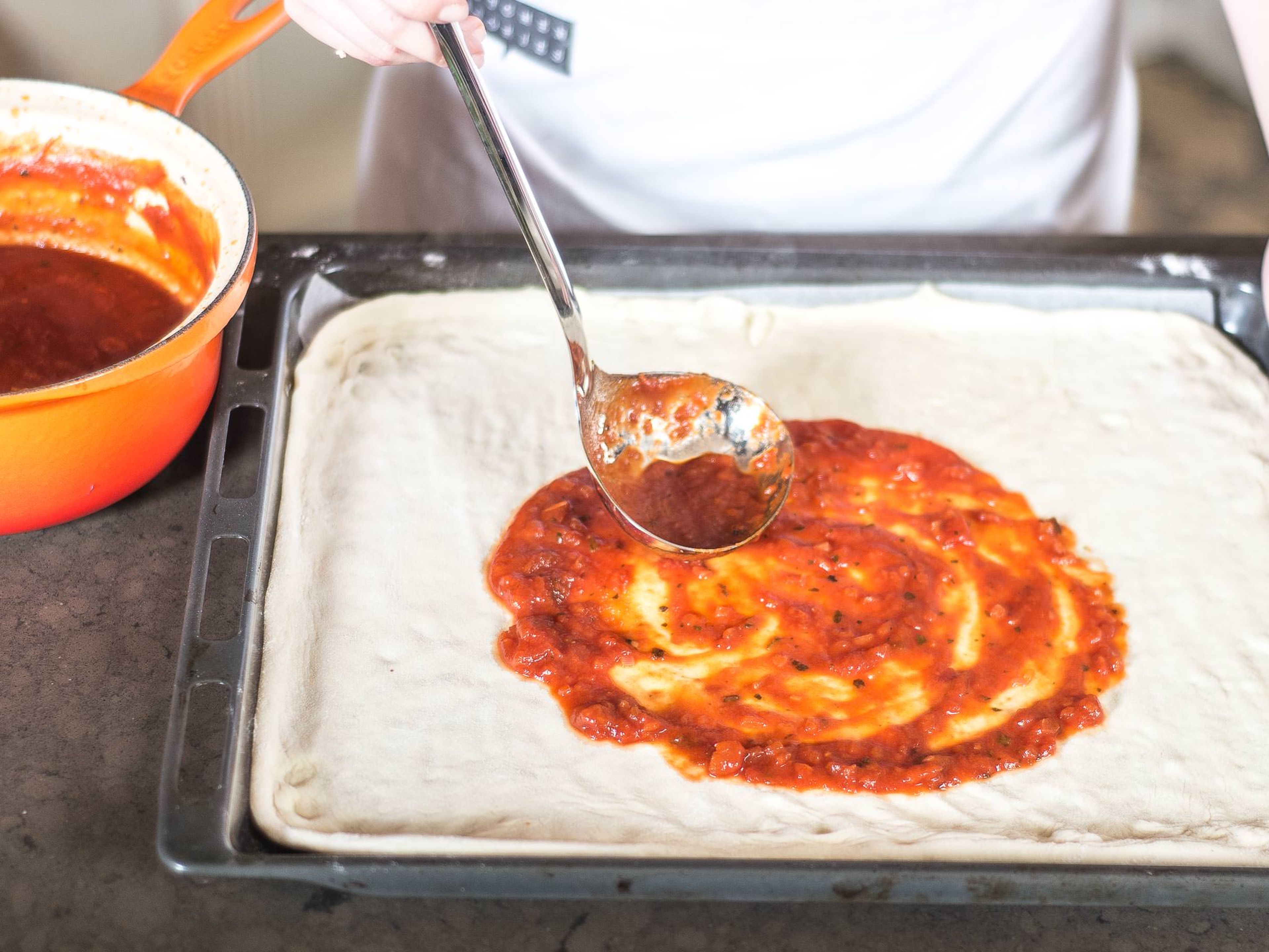 Using a ladle, spread the tomato sauce evenly on the dough.