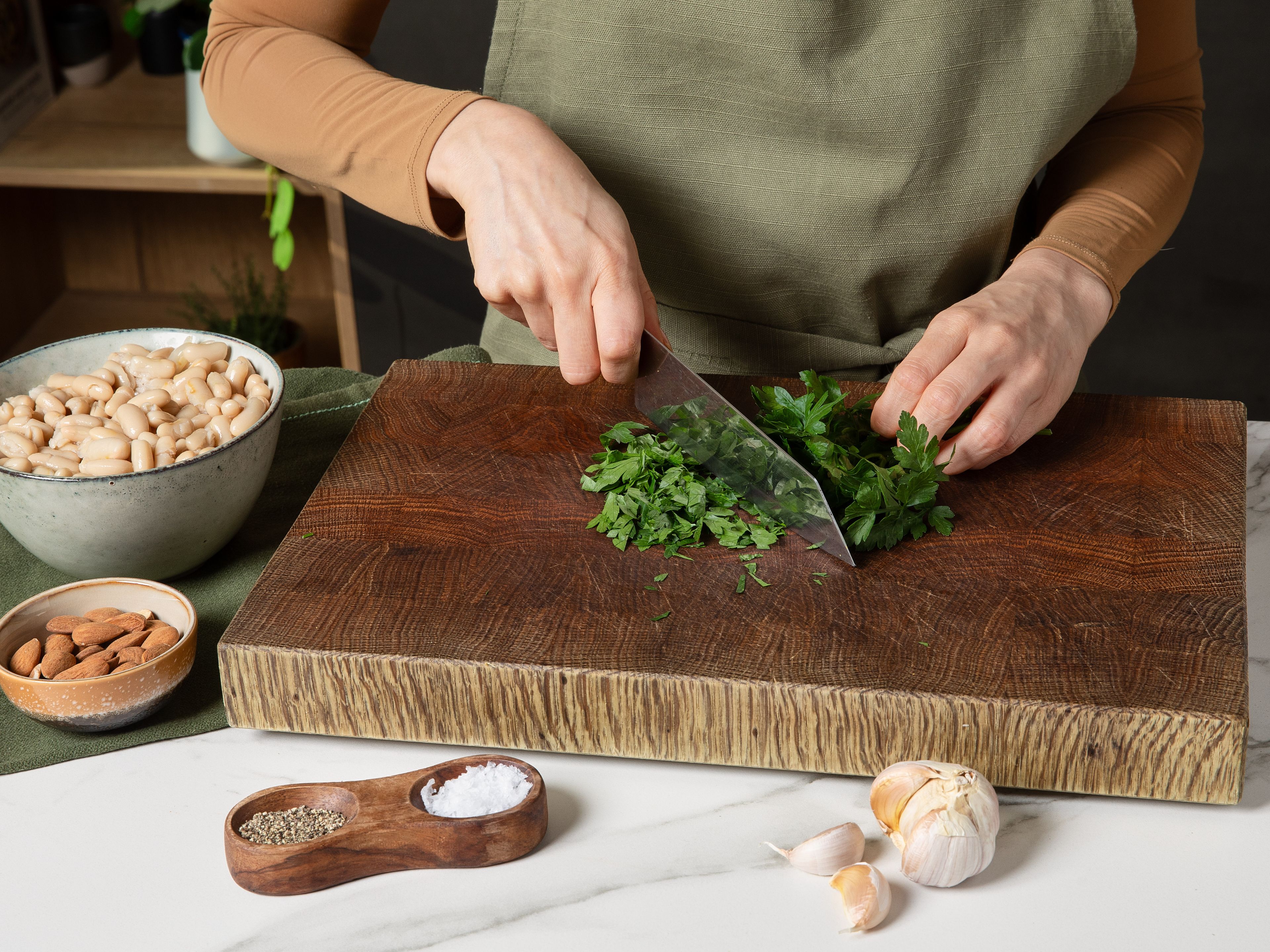 Die Bohnen aus der Dose abgießen und abtropfen lassen. Petersilie und Knoblauch fein hacken. Die Mandeln fein hacken und in einem mittleren Topf ohne Öl goldbraun rösten, herausnehmen und in einer kleinen Schüssel beiseitestellen.