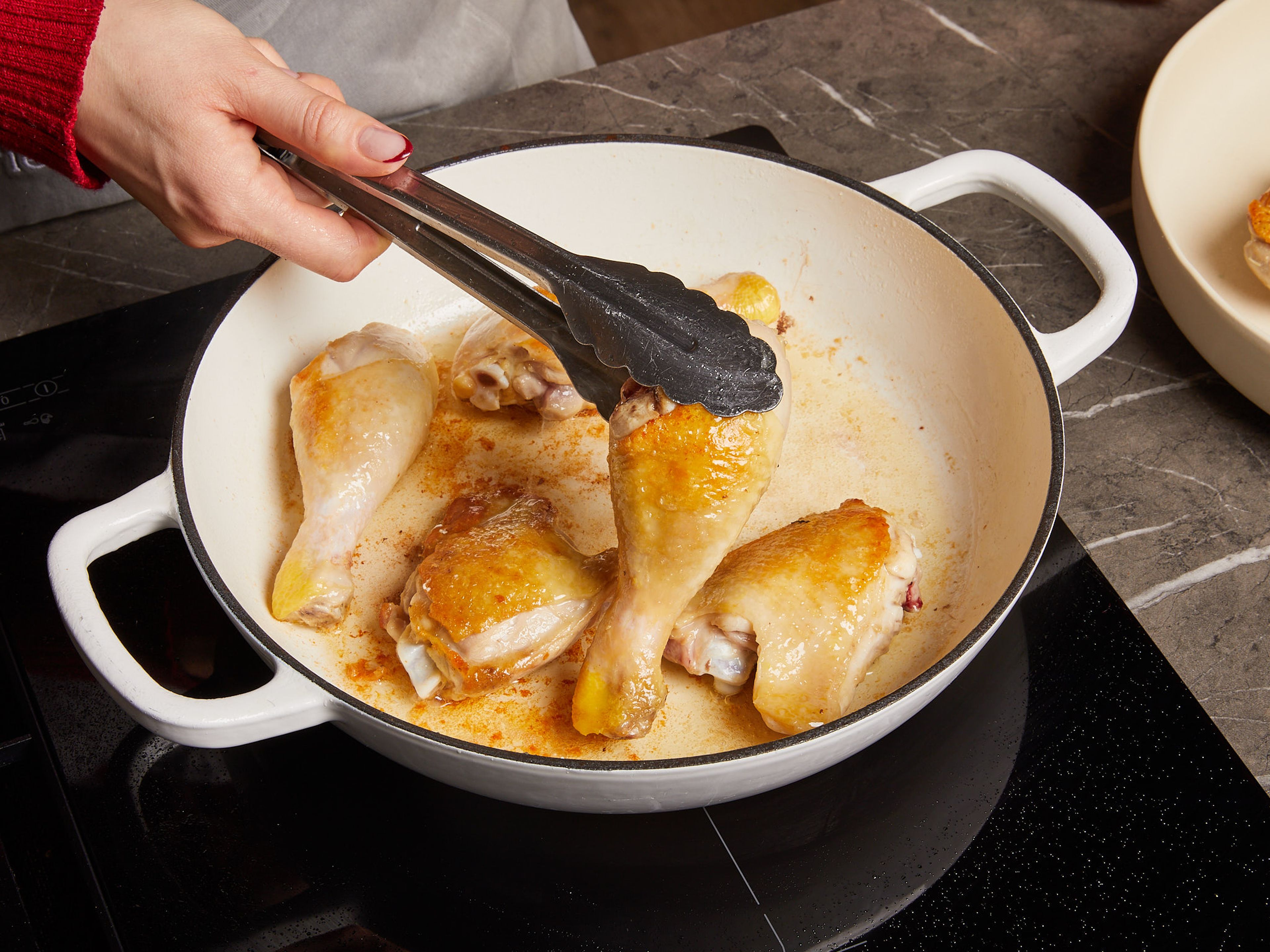 Ein wenig Öl in einer großen Pfanne erhitzen. Die Hähnchenschenkelstücke salzen und von allen Seiten anbraten, bis das Fleisch auf beiden Seiten goldbraun ist. Dann das Fleisch aus der Pfanne nehmen.