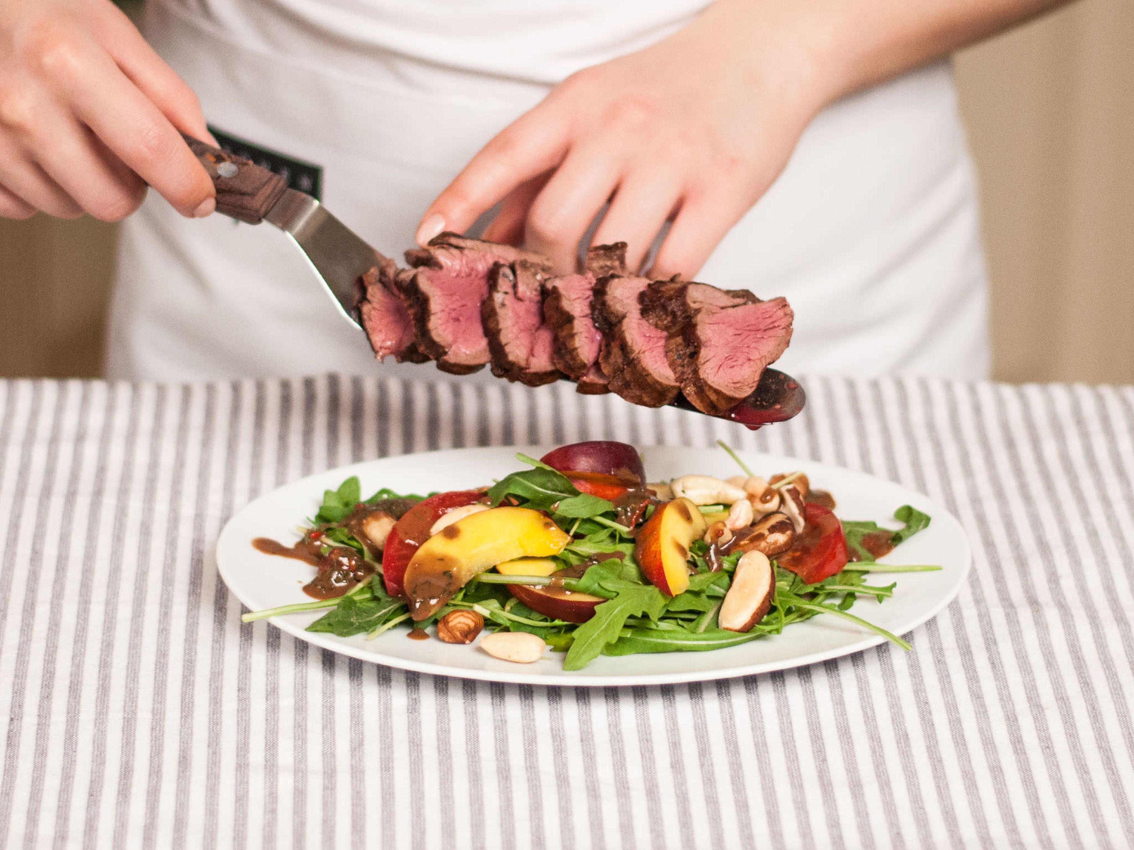 In a salad bowl, toss arugula, tomatoes, and nectarines with the dressing and place on serving plates. Slice up tenderloin and arrange on top of the salad. Sprinkle with toasted nuts and season again with salt and pepper before serving.