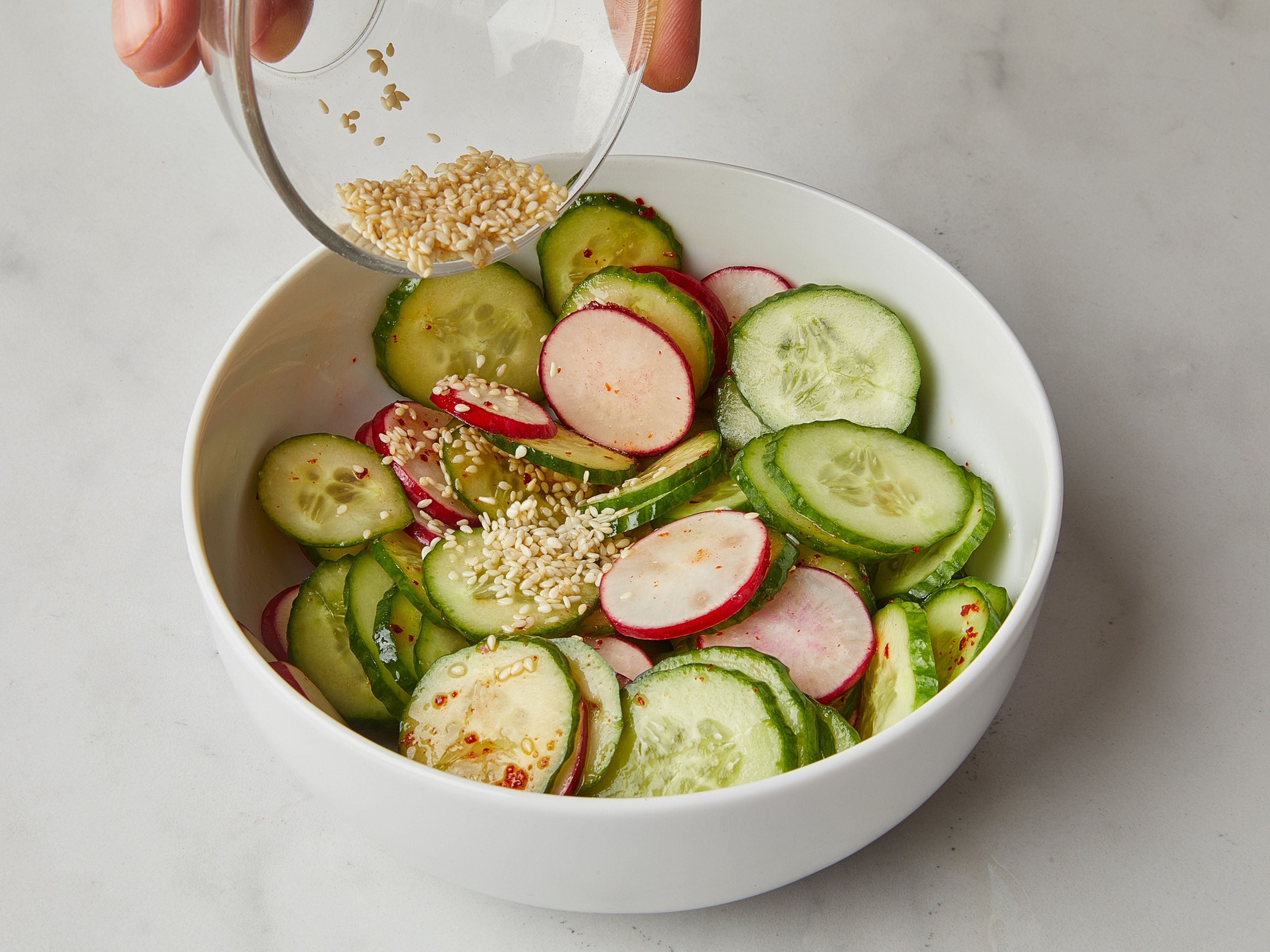 Thinly slice cucumber and radishes with a mandoline, add to a bowl. Add salt, rice vinegar, chili flakes, sesame oil, remaining sugar and sesame seeds, mix to combine and set aside.