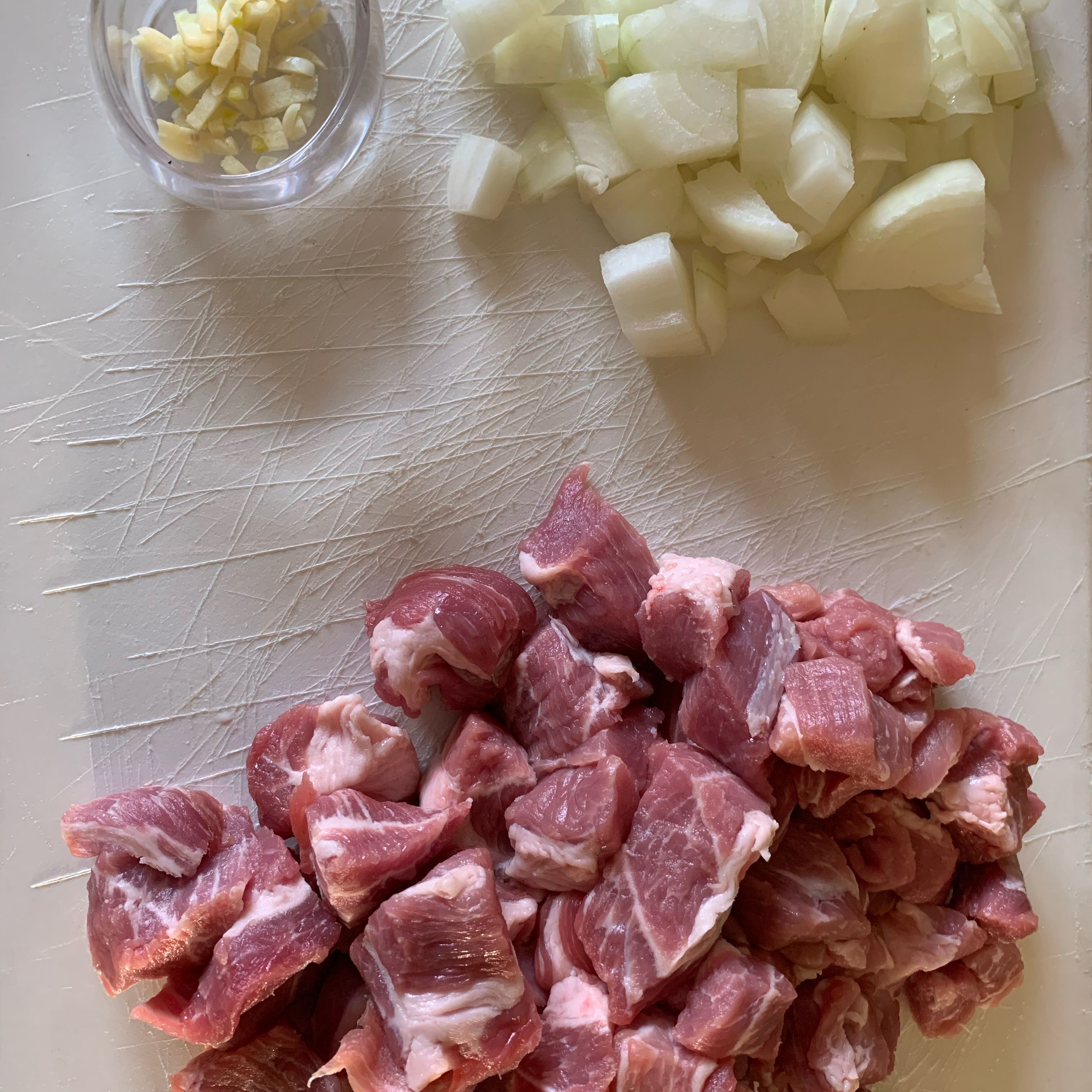 Zuerst die Zwiebeln würfeln (die Stücke müssen nicht zu fein sein), danach den Knoblauch in kleine Stücke schneiden. Das Schweinefleisch in ca 3 cm große Stücke schneiden.