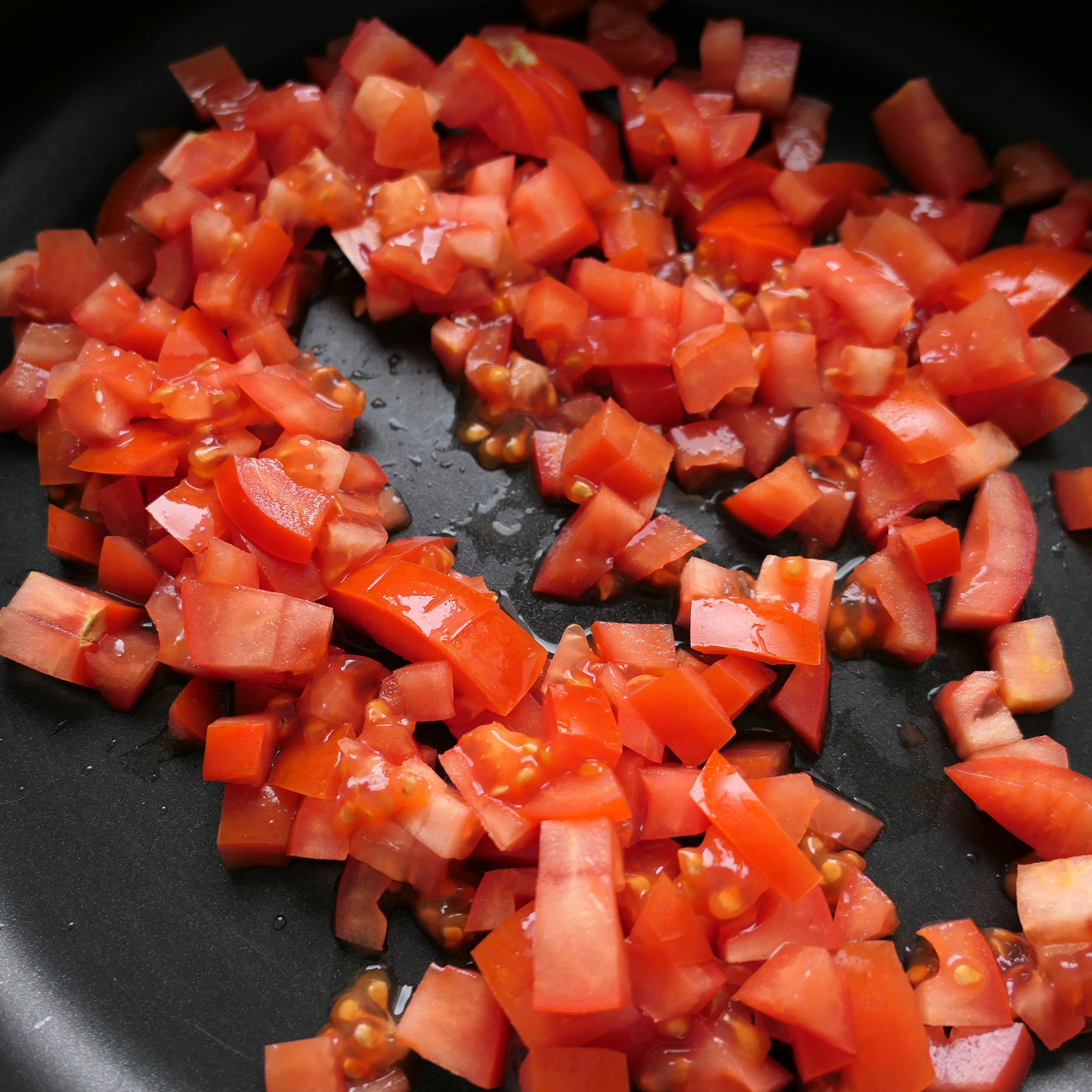 Würfle die Tomaten und brate sie bei mittlerer Hitze mit 1 EL Olivenöl in der Pfanne 10 Minuten an.