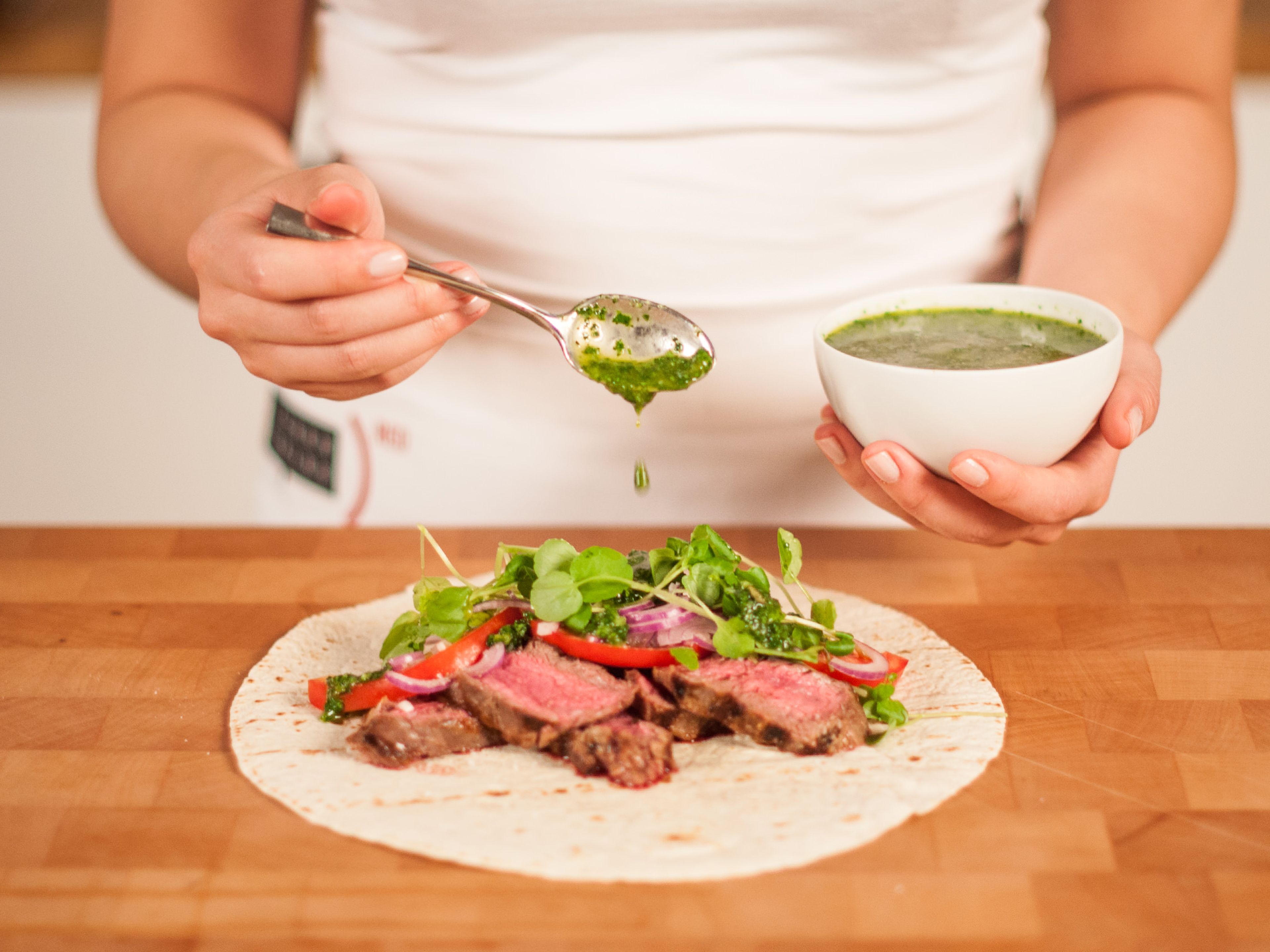Place sliced skirt steak on a tortilla. Add sliced tomato, sliced onion, and watercress. Then, drizzle with chimichurri. Fold and serve with more chimichurri.