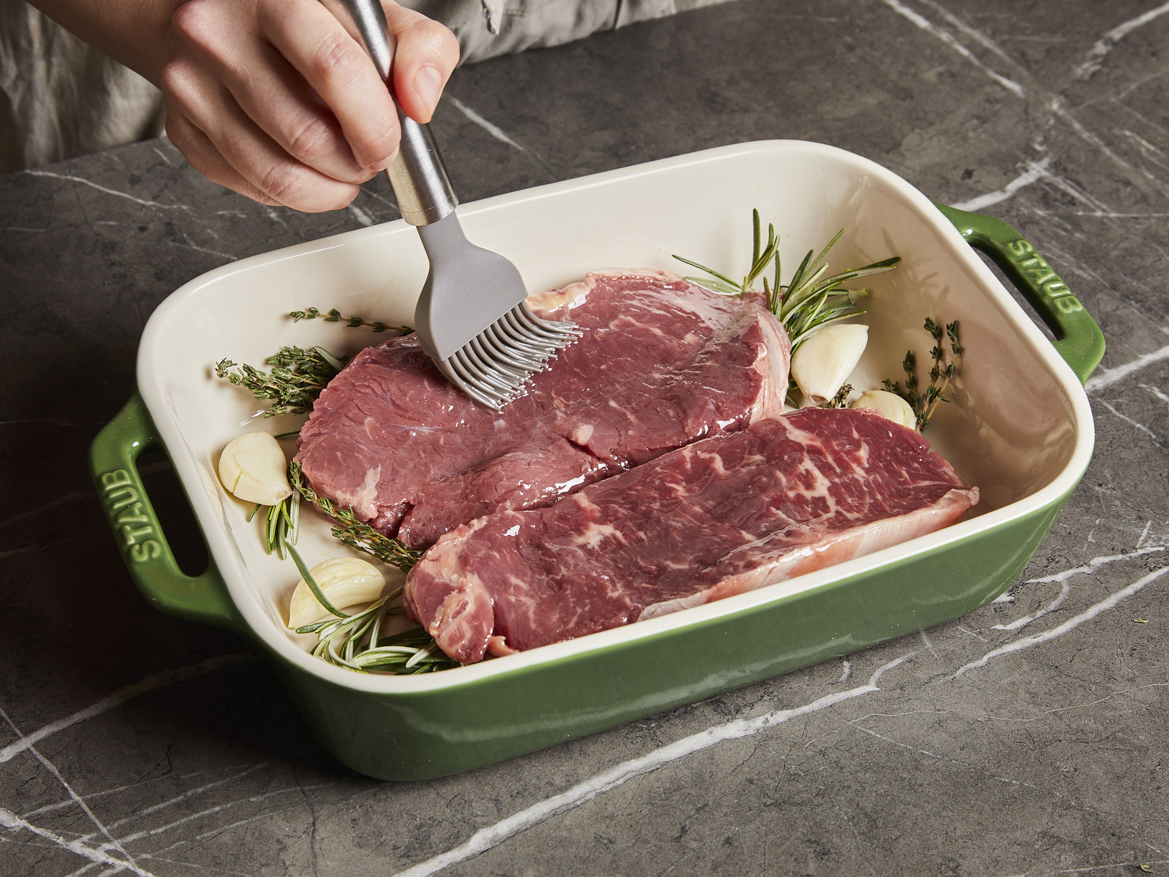 Brush the steaks with a little oil, season with salt and pepper and place in a baking dish with the herbs and peeled garlic cloves. Cook the steaks in the oven for approx. 50–60 min. or until the core temperature reaches the desired doneness (approx. 54–55°C/129–131°F for medium).