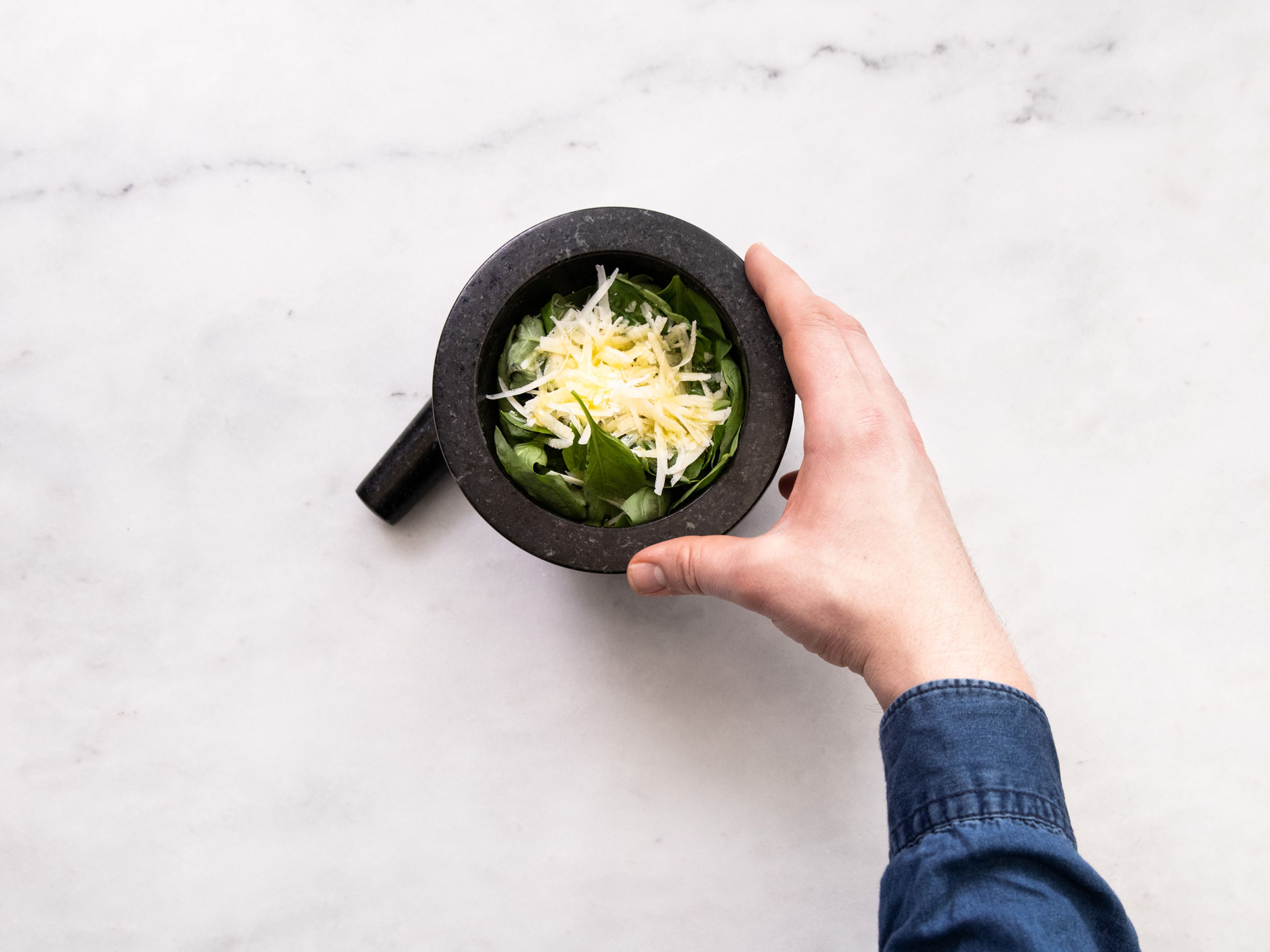 Add toasted pine nuts to a mortar. Add salt, pepper, and garlic and pound with the pestle. Add basil, shredded Parmesan cheese, and some olive oil and smash together to form the pesto. Set aside.