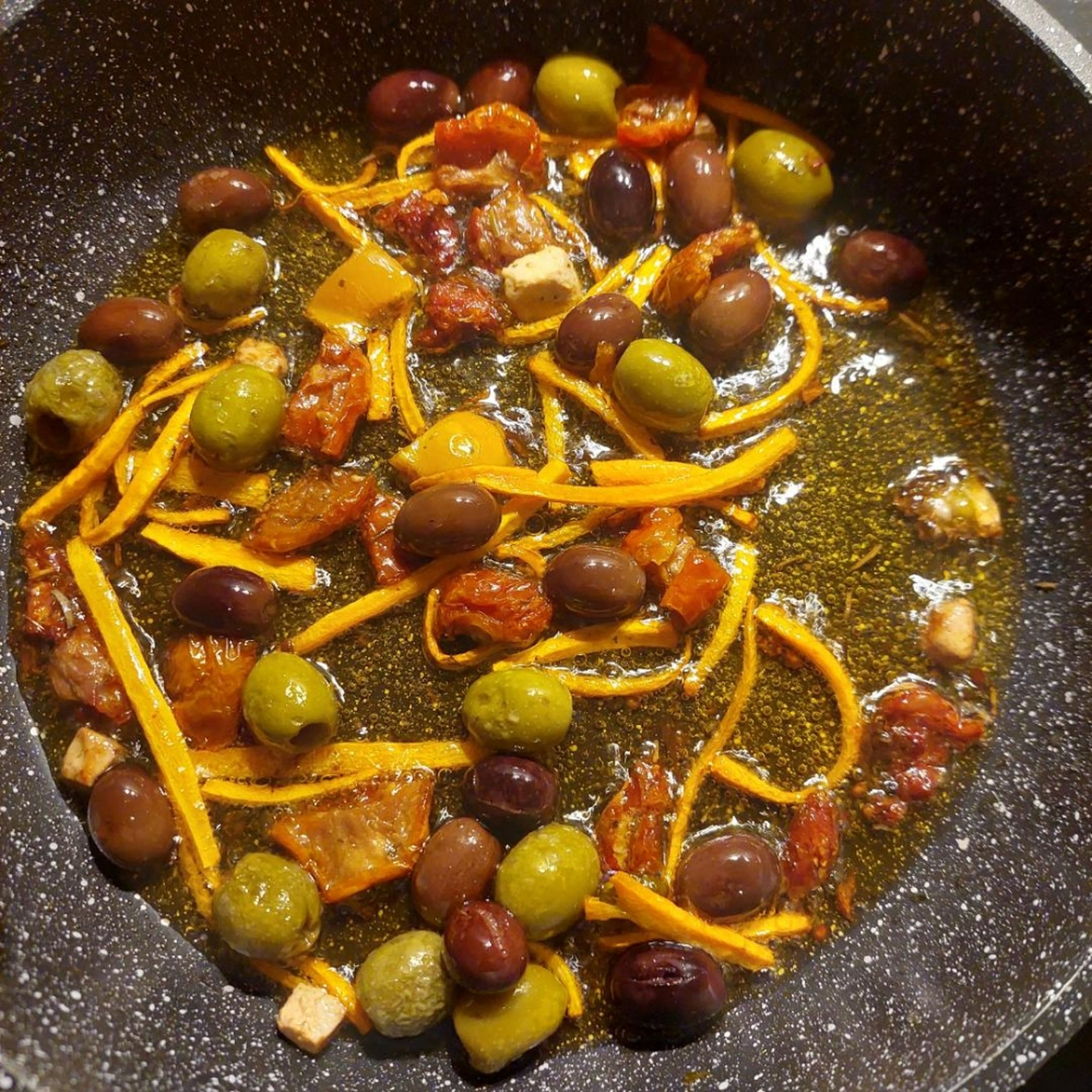 Öl von den getrockneten Tomaten in die Pfanne geben und heiß werden lassen. Getrocknete Tomaten, Feta und Karotte klein schneiden, hinzufügen und kurz mitbraten lassen. Oliven hinzufügen und alles auf hoher Stufe 5 Minuten braten.