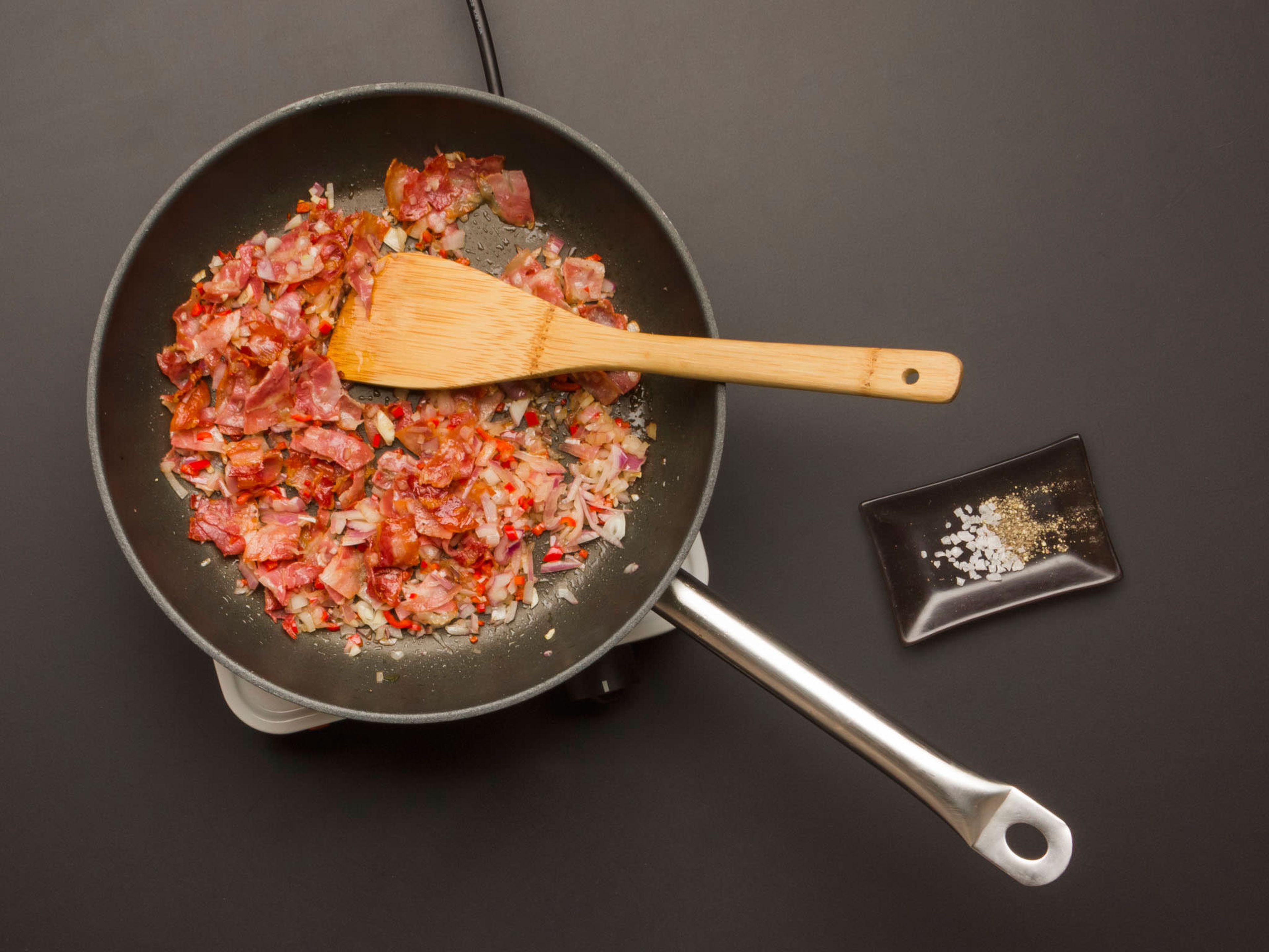 In same frying pan, cook pancetta over high heat for approx. 3 min. Then add garlic, onion, and peperoncino and continue to cook for another 2 min. over medium heat. Season to taste with salt and pepper.