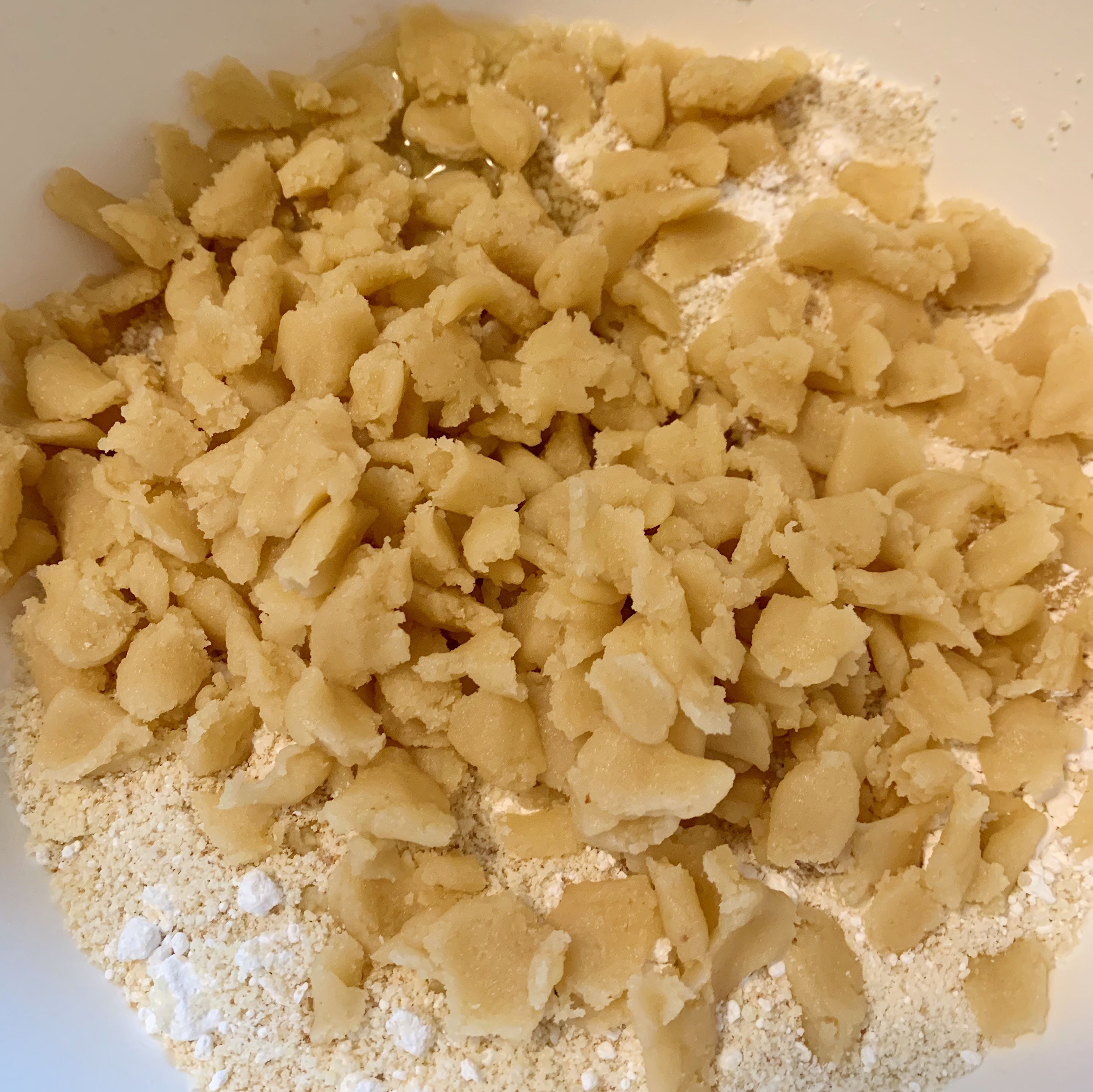 Eiweiß, Amaretto und Zitronenabrieb in die Schüssel geben. Marzipan-Rohmasse in kleine Stücke zupfen und ebenfalls zu den trockenen Zutaten geben. Alles mit den Händen zu einem glatten Teig verarbeiten.