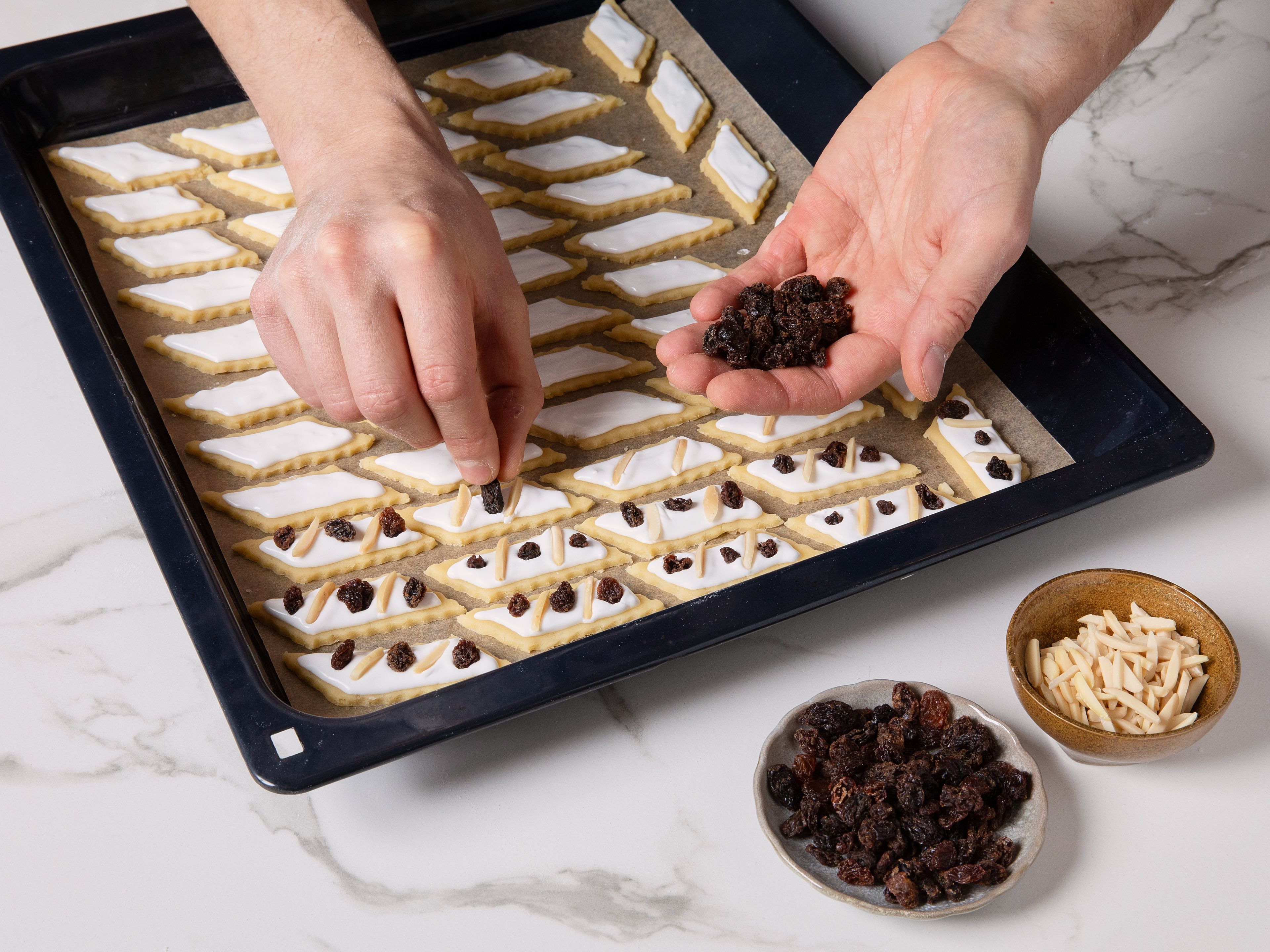 Brush cookies with the glaze. Decorate as desired with dried raisins and slivered almonds, and bake until golden yellow for approx. 10–14 min. Once they're done, carefully remove them from the sheet and let cool completely on a wire rack.