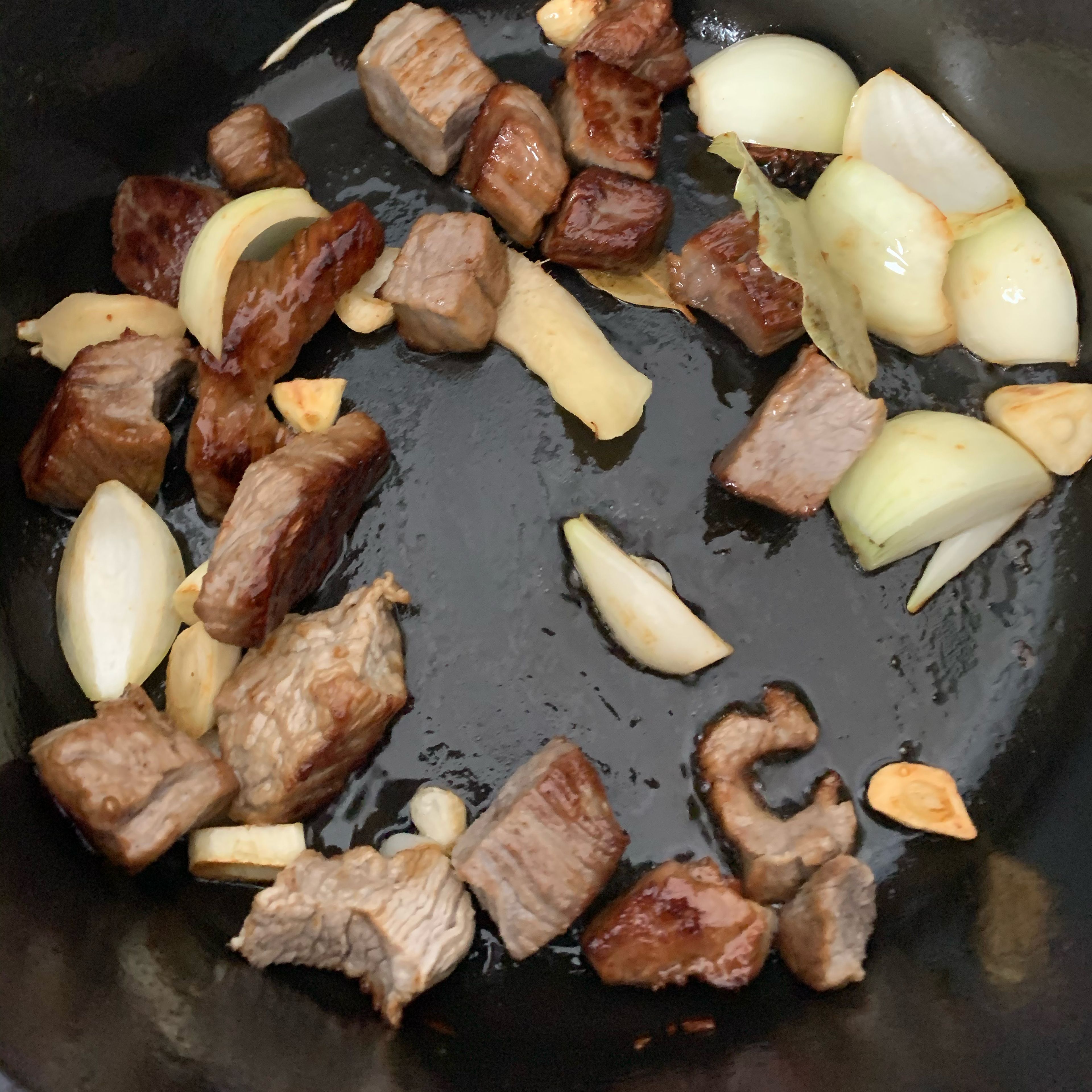 In cast iron pot, add vegetable oil. Add rock sugar, heat over medium-low heat, until the sugar melts. Then add beef, stir so the beef is coated. Then add onion, star anise, bay leaves, dried chilli, garlic and 3 slices ginger. Stir fry for approx 2 min..