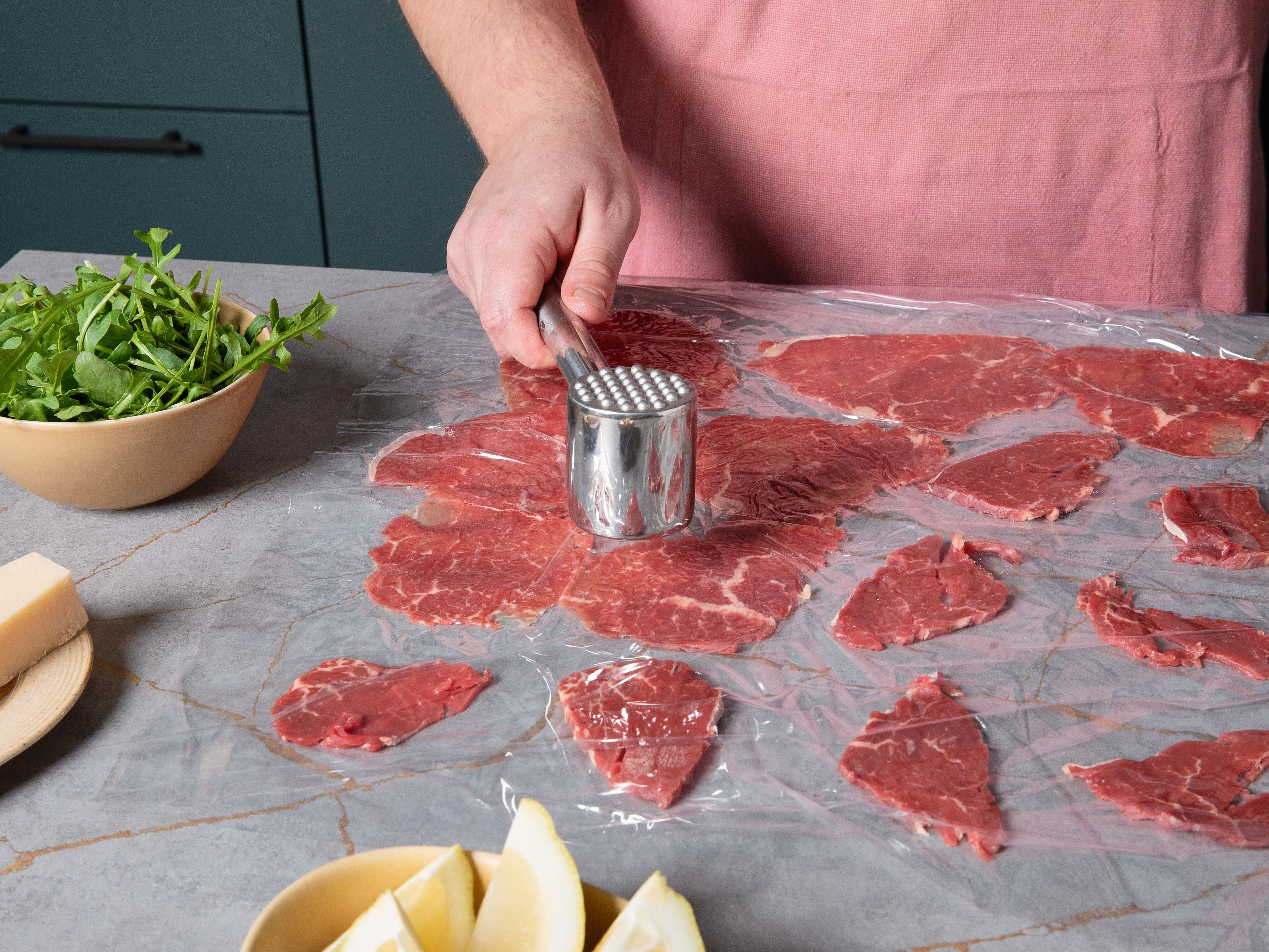 Die dünnen Fleischscheiben auf Frischhaltefolie ausbreiten, dabei zwischen den Stücken etwas Platz lassen. Eine zweite Lage Folie darüber legen. Das Fleisch nun mit einem Fleischklopfer oder dem Boden einer Pfanne vorsichtig auf ca. 1 mm Dicke platt klopfen.