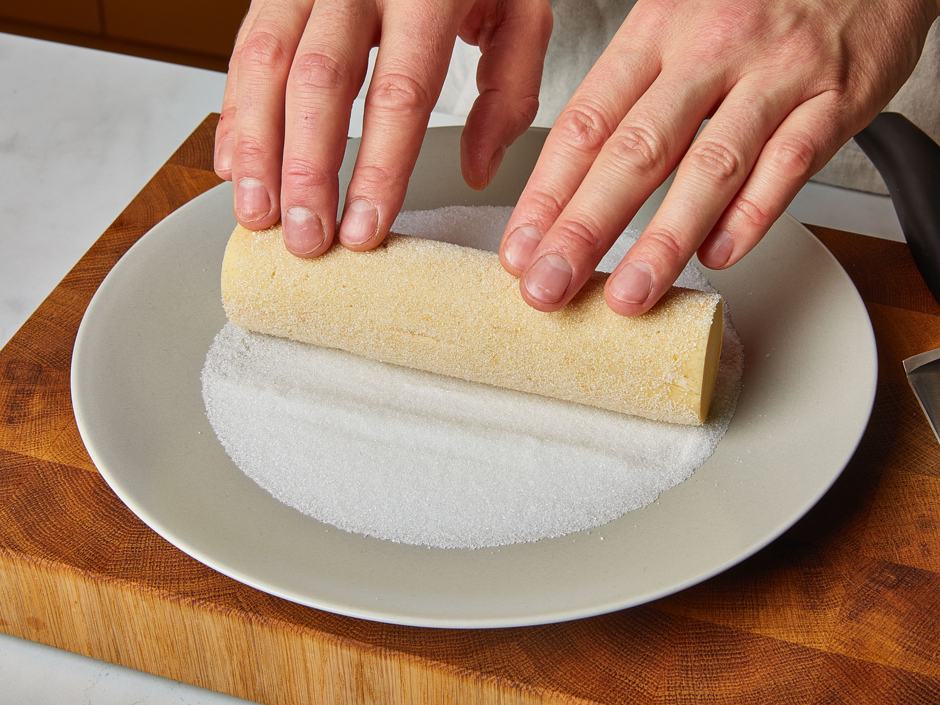 Zum Backen der Plätzchen den Ofen auf 170°C vorheizen. Den Teig herausnehmen und die Plastikfolie entfernen. Etwas Zucker in einen tiefen Teller streuen. Die Teigrollen gleichmäßig im Zucker wälzen, damit die Ränder nach dem Backen besonders knusprig werden.