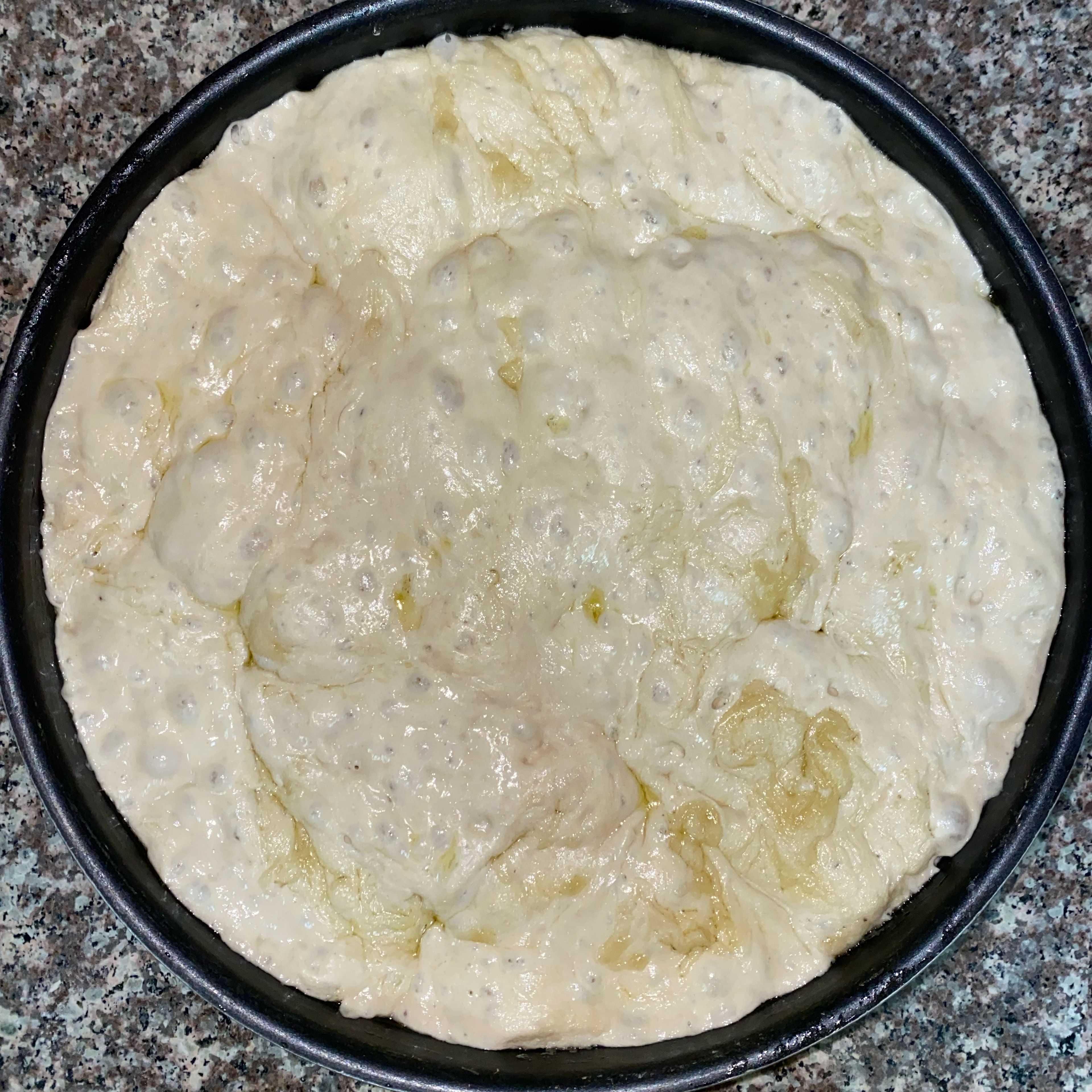 Using a rubber spatula, gently stir a tablespoon of olive oil into the dough until well combined and cover with plastic wrap again, setting it aside to proof for an additional 2 hours.