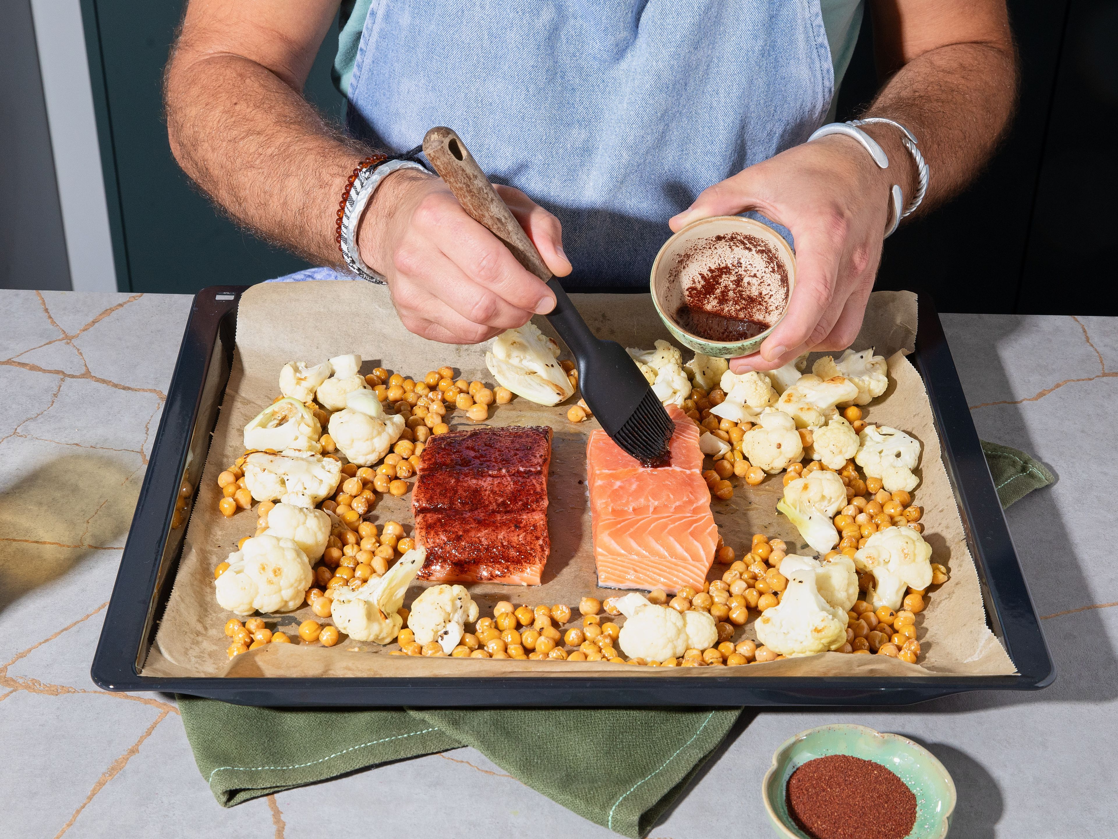 Meanwhile, mix sumac with olive oil and season with salt. Rub flesh of salmon with the mix. After approx. 15 min. baking time, take baking sheet out of oven and shake to flip cauliflower and chickpeas. Make space in the center and add salmon skin-side down onto the tray. Bake everything for approx. 10 min. more. Make sure salmon reaches approx. 50°C/120°F internal temperature and cauliflower and chickpeas get crispy.