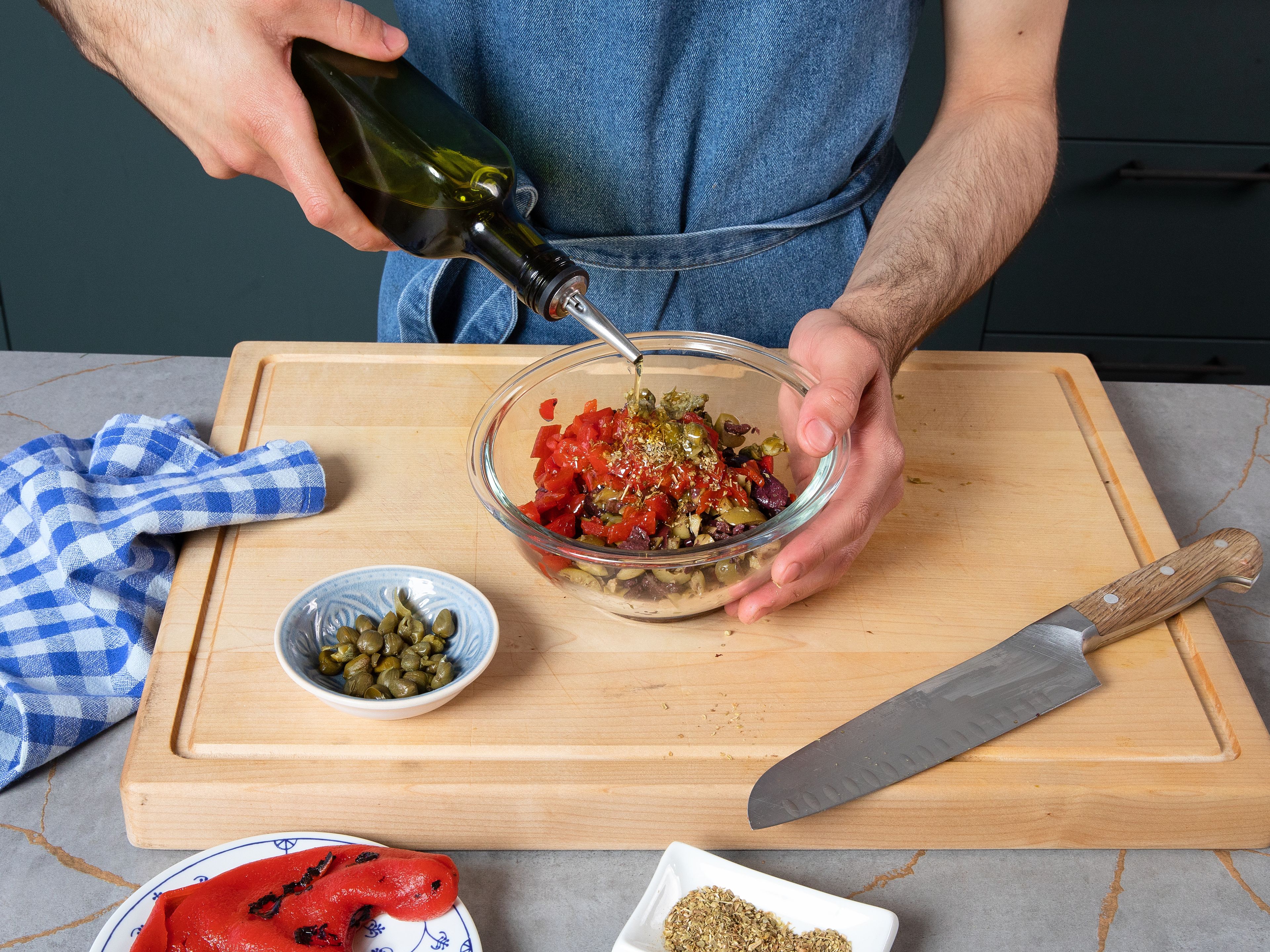 Roughly chop olives, jarred roasted bell pepper, and capers together. Add to a bowl and mix chopped goods with olive oil, oregano, and a pinch of salt.