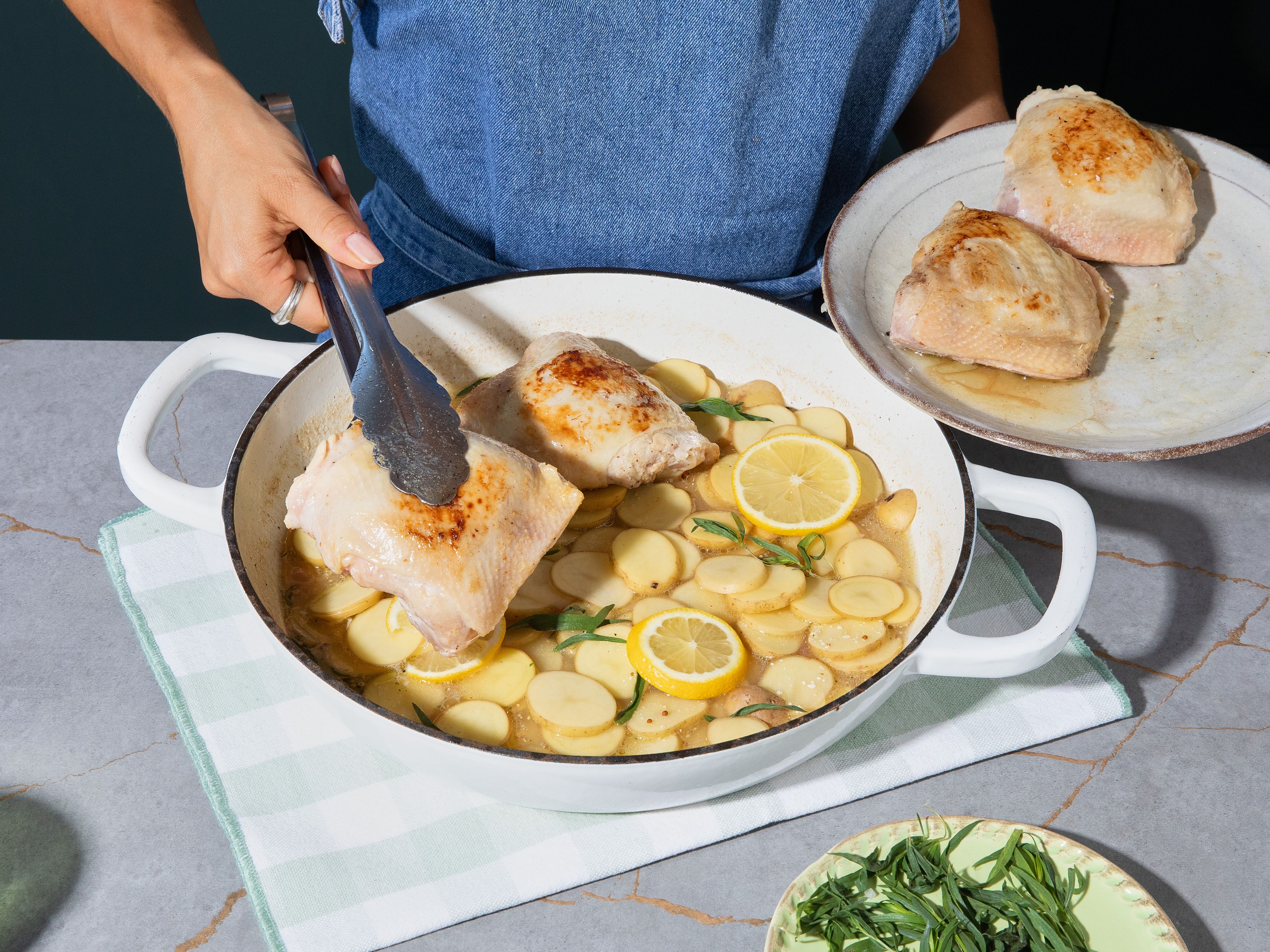 Slice parboiled potatoes and arrange in skillet on top of sauce. Place lemon slices on top and arrange chicken thighs over potatoes. Bake in preheated oven for approx. 35–40 min., until potatoes are tender and chicken is cooked through. Sprinkle with cornichon-parsley mixture and serve immediately.