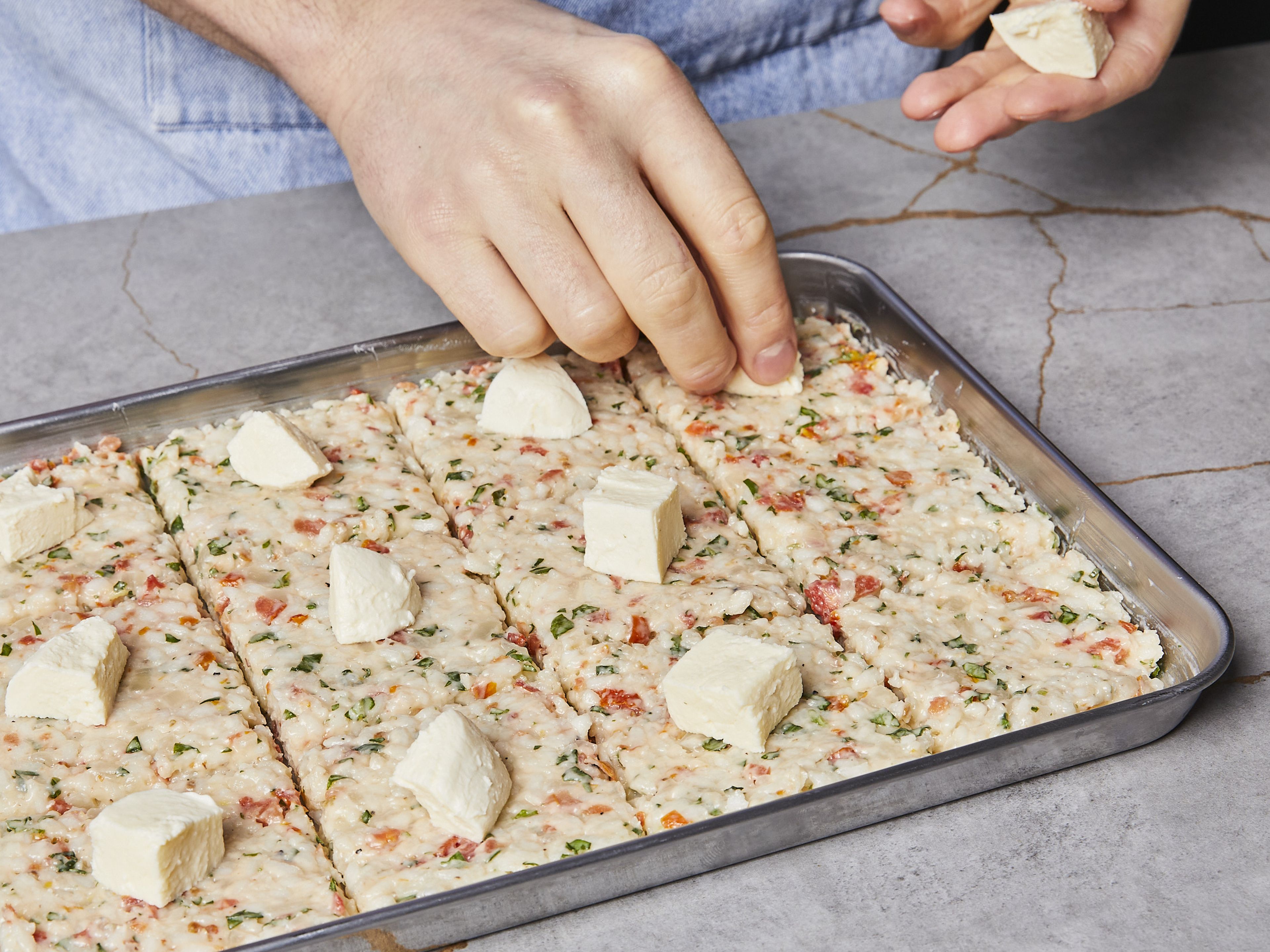 Den Mozzarella in kleine Würfel schneiden. Zum leichteren Portionieren mit einem Messer ca. 7 cm x 7 cm große Quadrate in den Reis schneiden. Auf jedes Quadrat ein Mozzarella-Stück legen. Mit feuchten Händen den Risottoreis zu Kugeln um jedes Mozzarella-Stück formen.