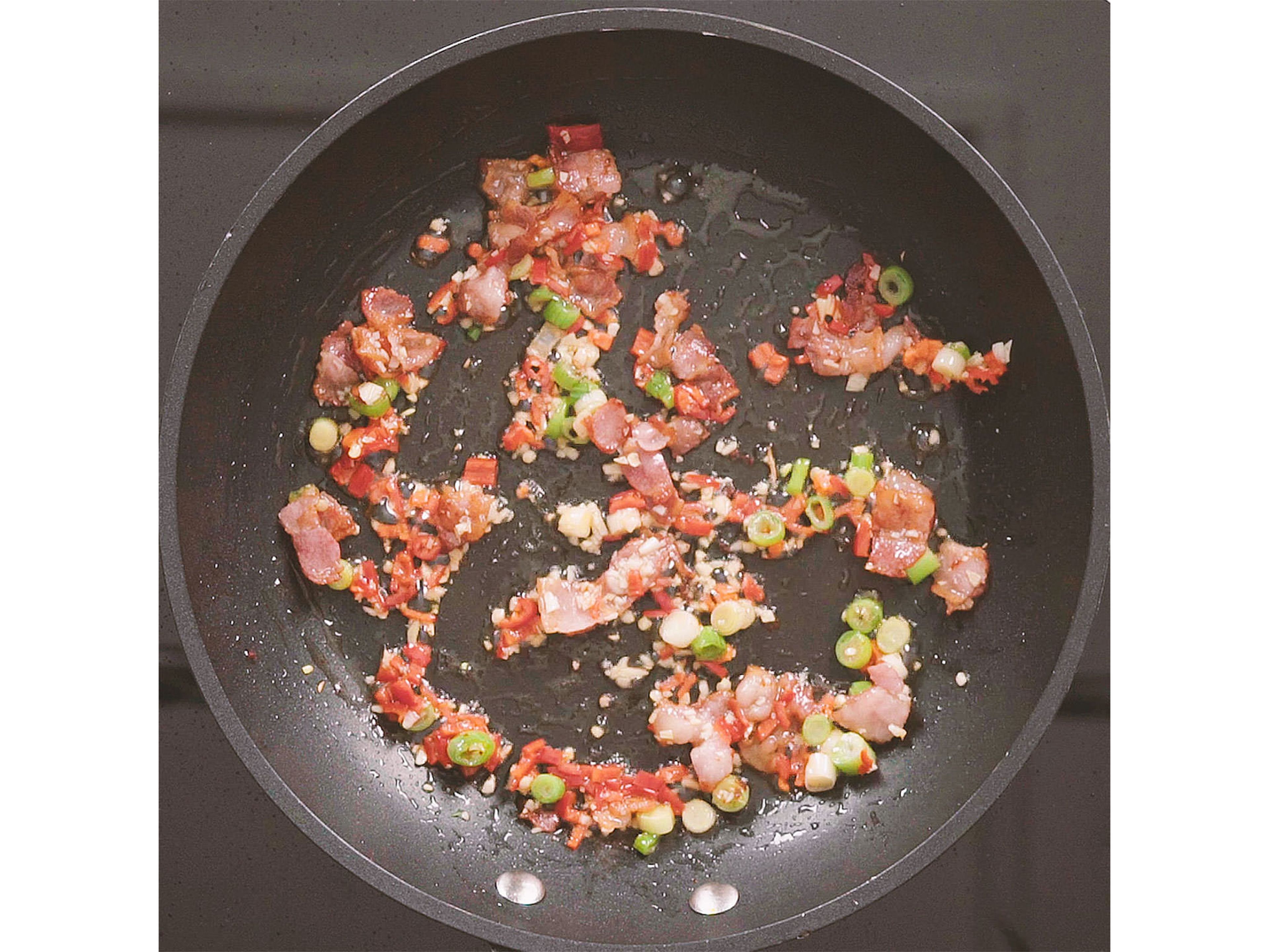 Add sesame oil, then add scallion whites, minced garlic, and chili to bacon and sauté for approx. 1 min. or until fragrant.