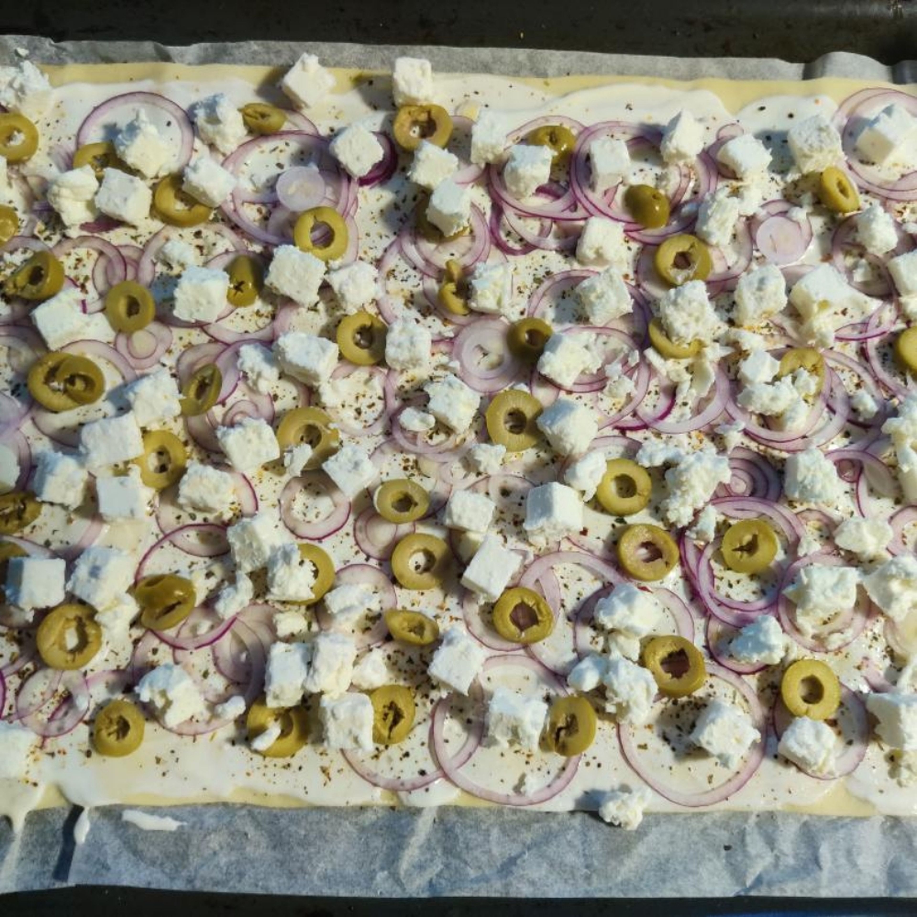 Zwiebeln, Oliven und Feta auf dem Blech verteilen, und dann 15 Minuten im Ofen backen.