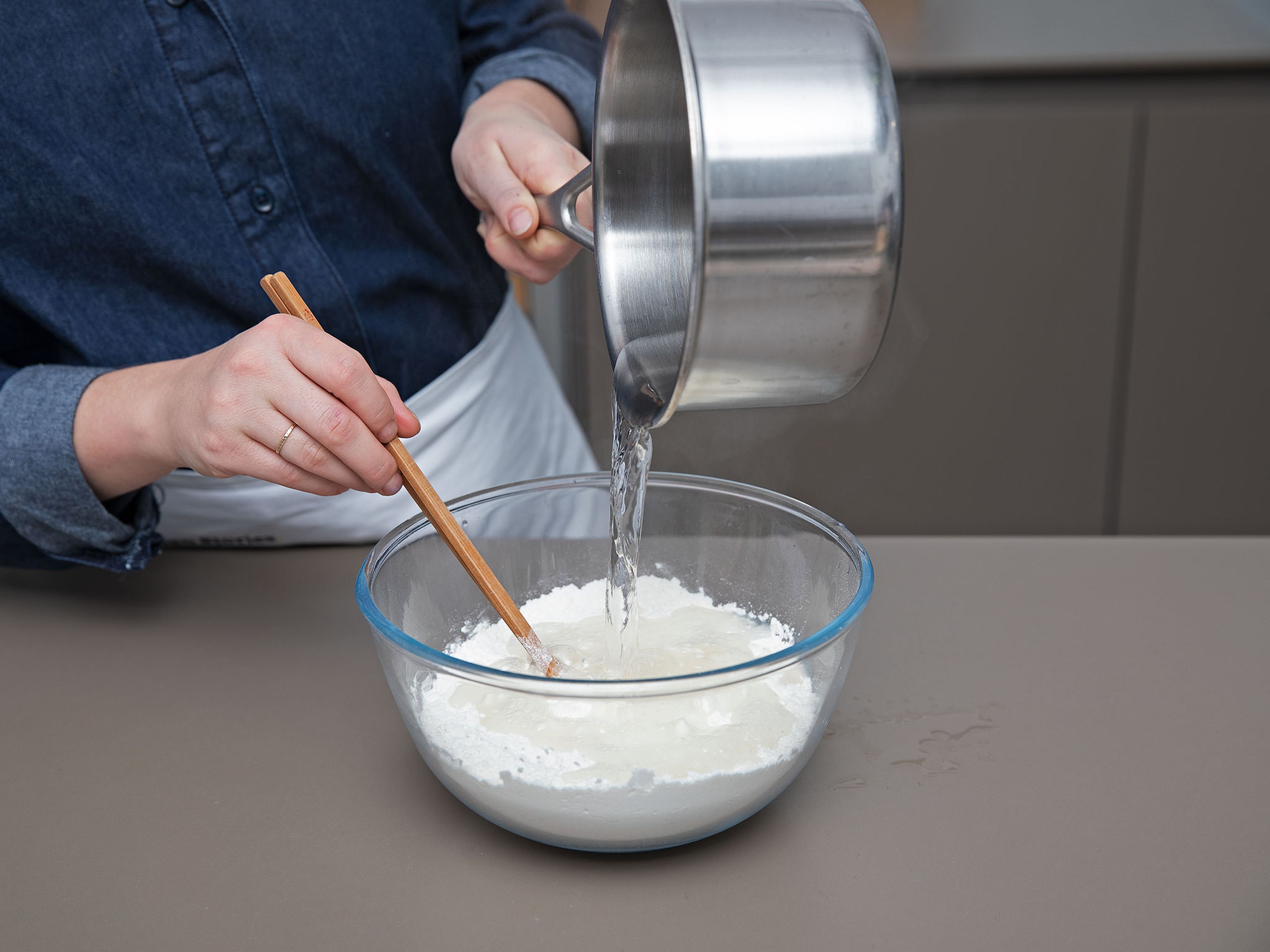Für die Mandarin-Pfannkuchen Wasser  in einem Topf zum Kochen bringen. In einer Schüssel Mehl mit Salz vermengen, mit dem kochenden Wasser übergießen und mit Stäbchen verrühren. Sobald die Teigmasse abgekühlt ist, ca. 8 Min. kneten, oder bis ein geschmeidiger Teig entsteht. Mit einem Geschirrtuch bedecken und ca. 1 Std. ruhen lassen.