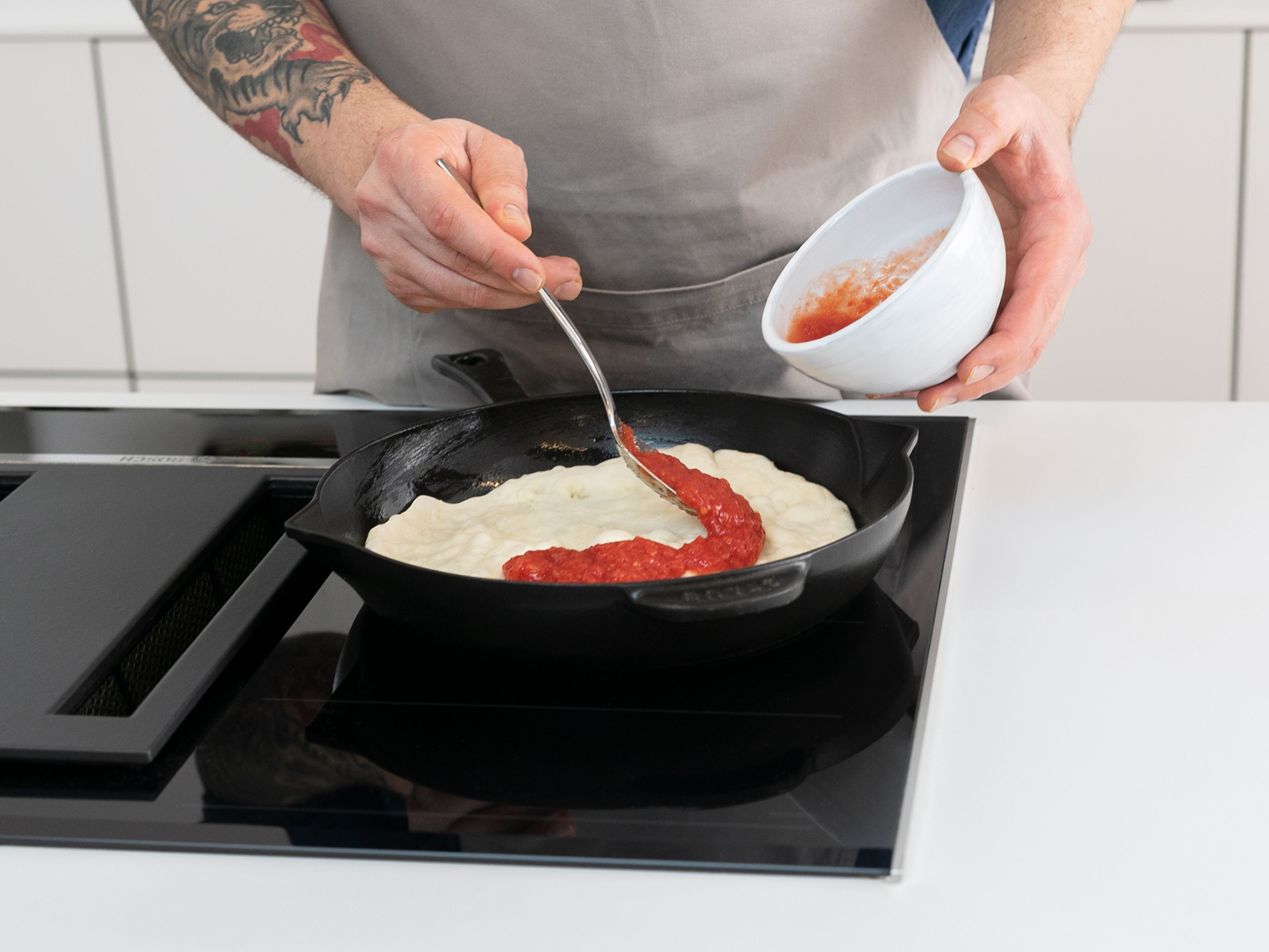 Once the dough has rested, preheat the oven to 250°C/480°F and move a rack to the highest position. Knead dough lightly on a lightly-floured work surface until it’s about the size of the cast iron skillet you will use to cook the pizza. Set the cast iron skillet over medium-high heat. Once the skillet is hot, add remaining olive oil, then transfer crust to the skillet. Let cook for approx. 1 min., then spoon on the sauce evenly over the crust.