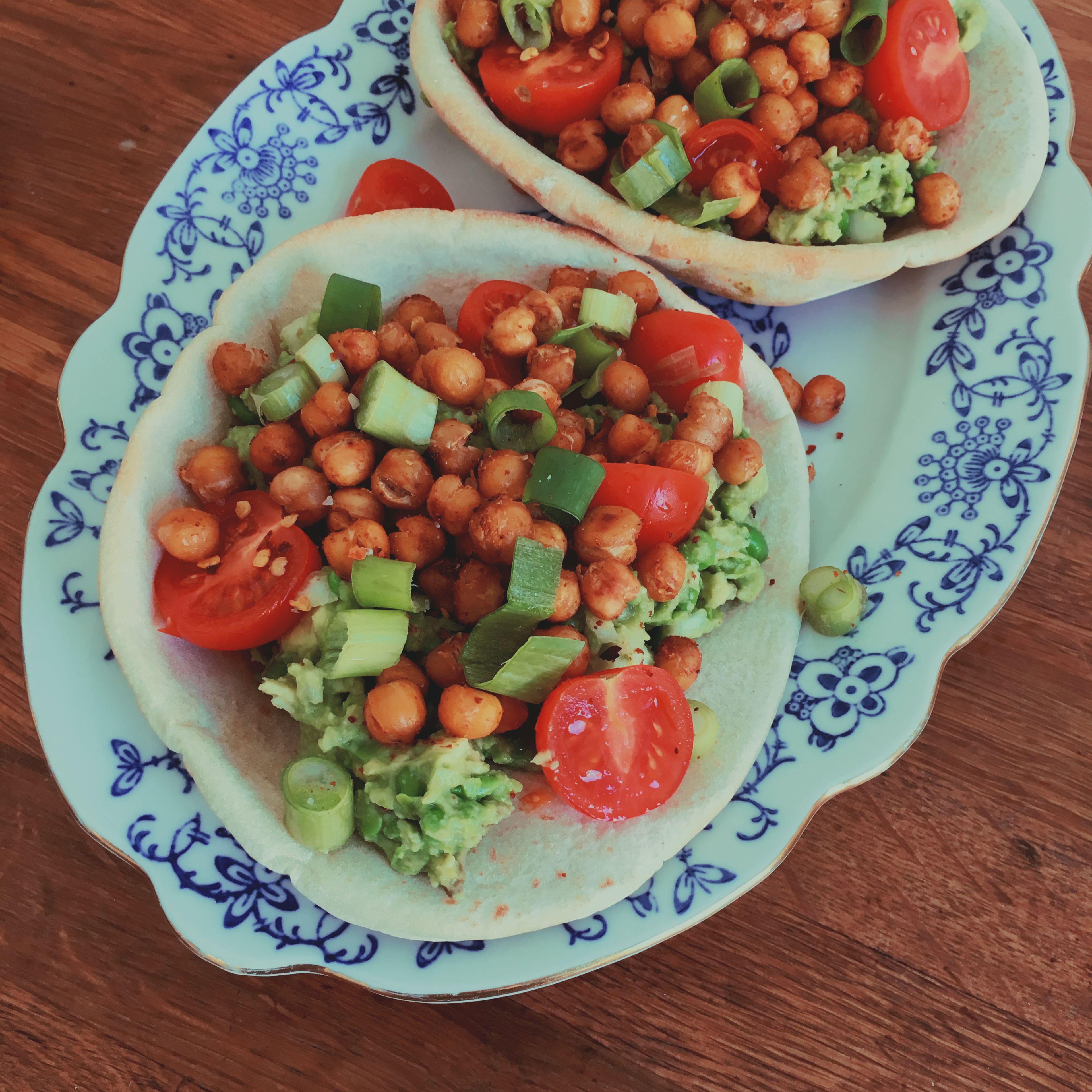 Fill pita breads with mashed green peas and avocado. Top with tomatoes, scallions, and crispy chickpeas. Enjoy!