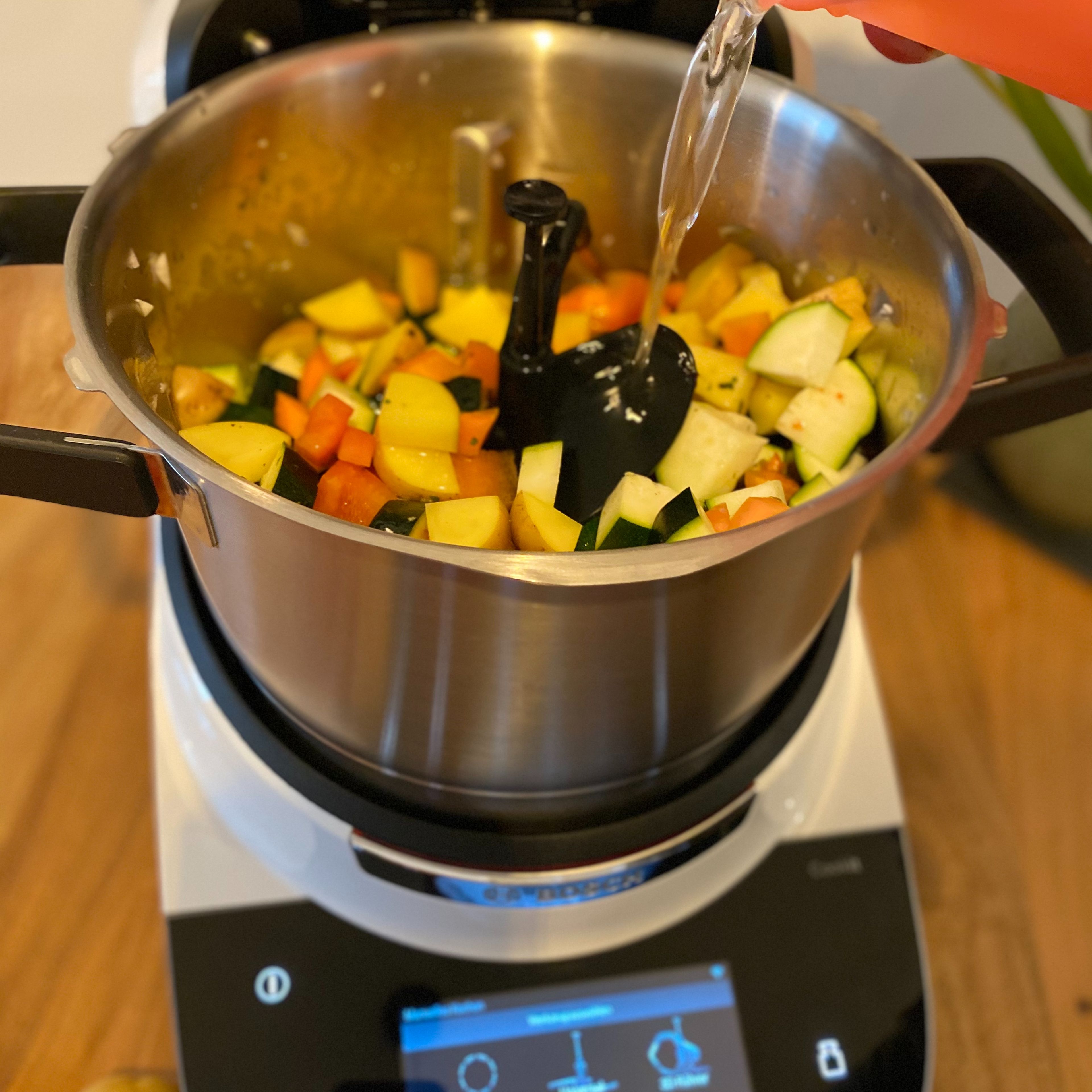 Das Gemüse, bis auf die Tomaten, zu der Zwiebel und dem Knoblauch geben. Alles mit reichlich Gemüsebrühe auffüllen und je nach Größe des Gemüses ca. 15 Minuten mit geschlossenem Deckel und eingesetztem Messbecher gar kochen lassen (3D-Rührer l Stufe 3 l 98°C l 15 Min.).