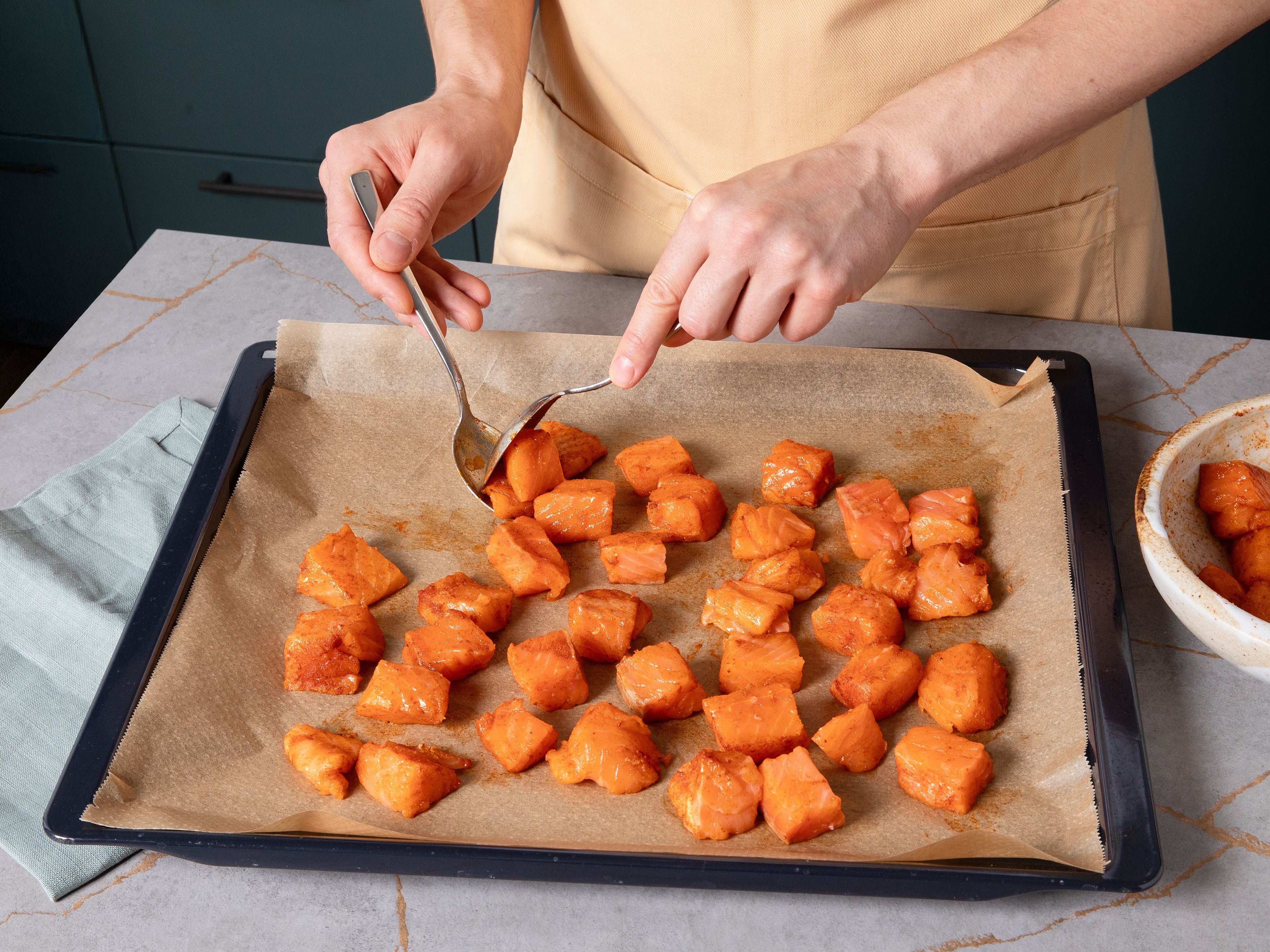 Ein Backblech mit Backpapier auslegen. Den gewürzten Lachs darauf verteilen, mit Öl beträufeln und im Ofen ca. 8–10 Min. backen, bis er gar ist und sich leicht zerteilen lässt. Währenddessen den Reis nach Packungsanleitung kochen. Währenddessen Rotkohl in sehr feine Streifen schneiden, Karotten schälen und raspeln.