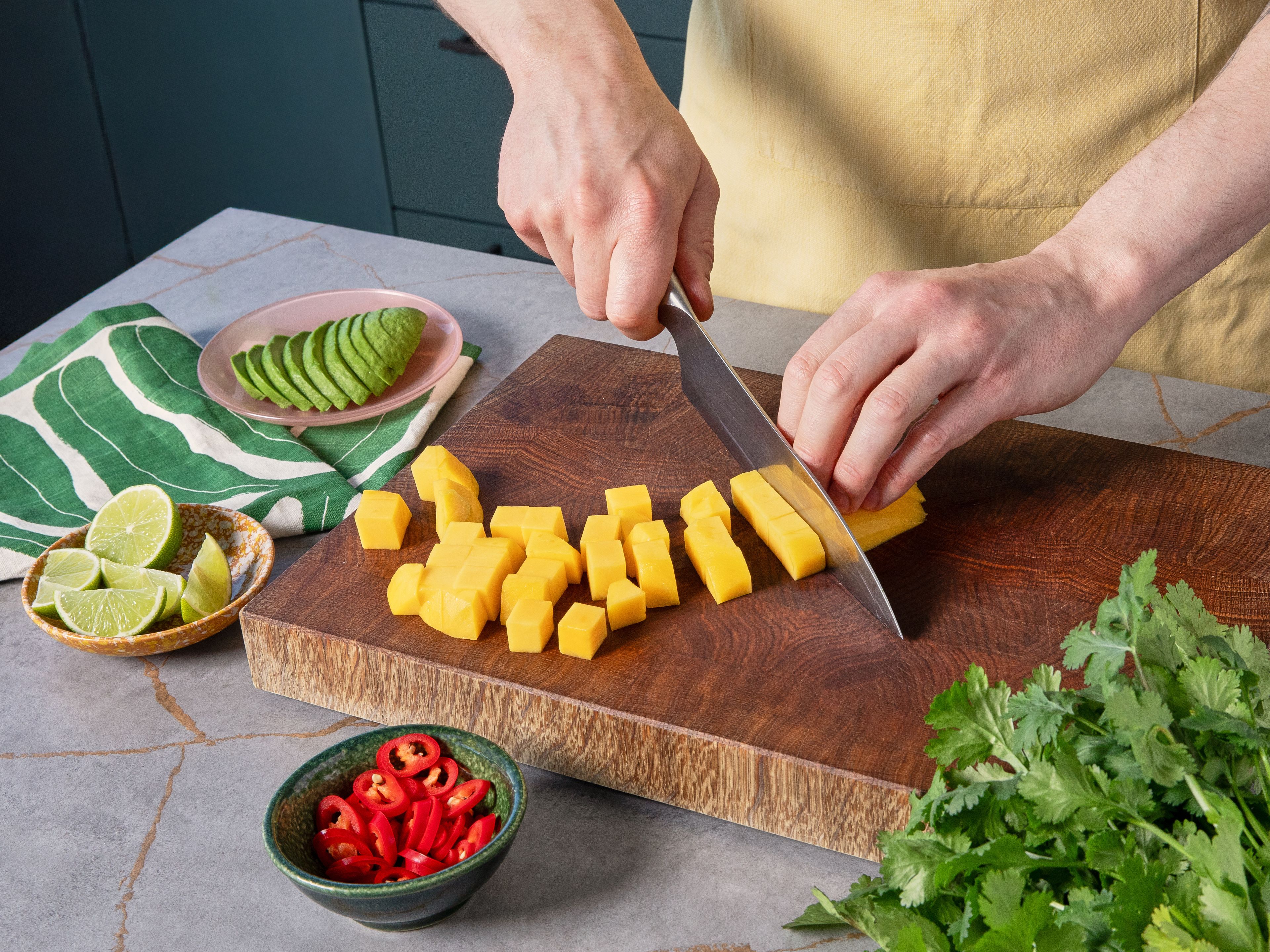 Die Mango schälen, das Fruchtfleisch vom Kern lösen und in kleine Würfel schneiden. Die Avocado halbieren, entkernen, Fruchtfleisch mit einem Löffel herauslösen und in Scheiben schneiden. Die Limette halbieren und Saft einer Hälfte über die Avocados träufeln. Die zweite Hälfte in Spalten schneiden. Eisbergsalat in feine Streifen schneiden, Koriander grob hacken. Die Chili entkernen und fein hacken.