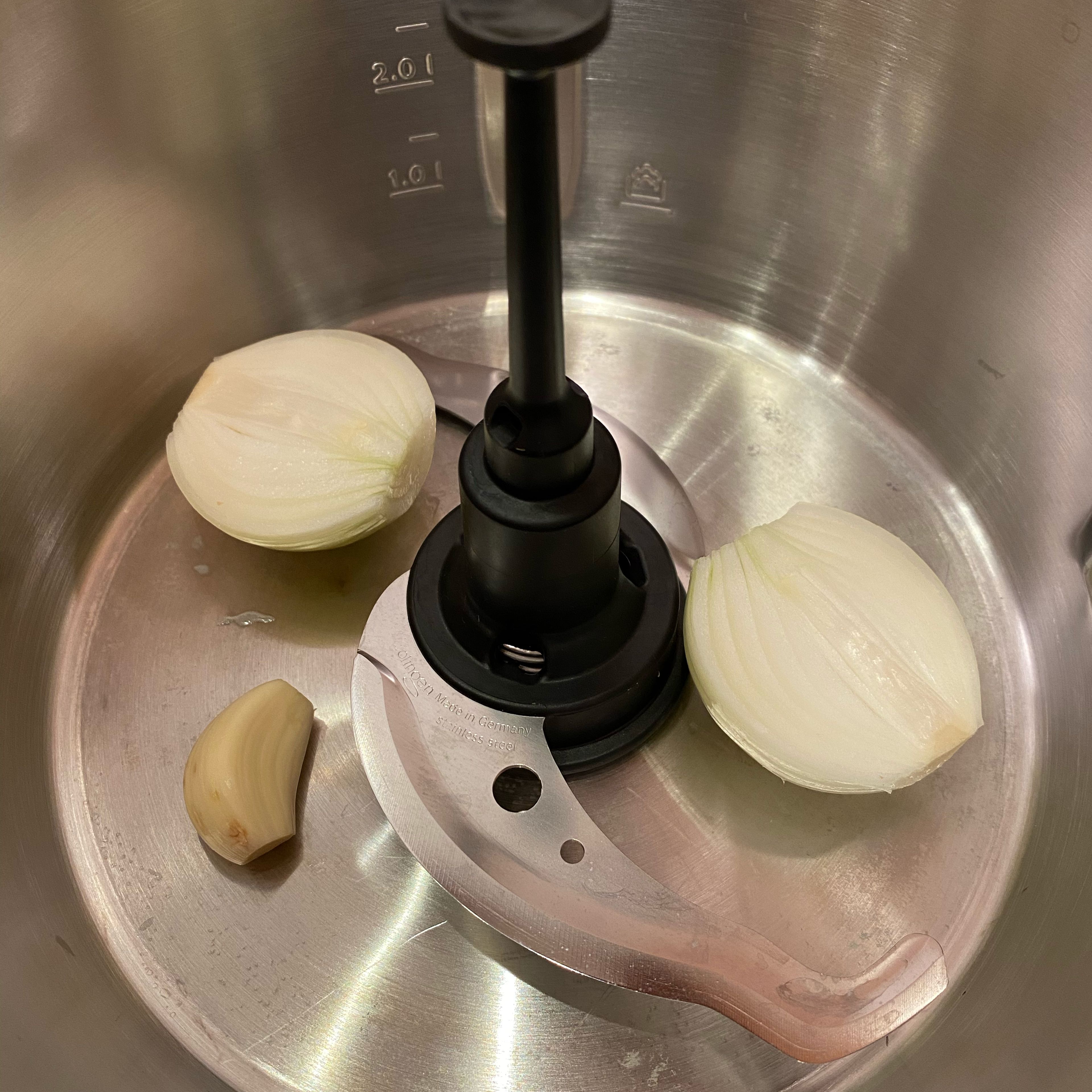 Universalmesser in den Mixtopf einsetzen, geschälte Knoblauchzehe und geschälte, halbierte Zwiebel hinzufügen, Deckel inkl. Messbecher schließen und zerkleinern (Universalmesser | Stufe 14 | 6 Sekunden). Universalmesser entnehmen.