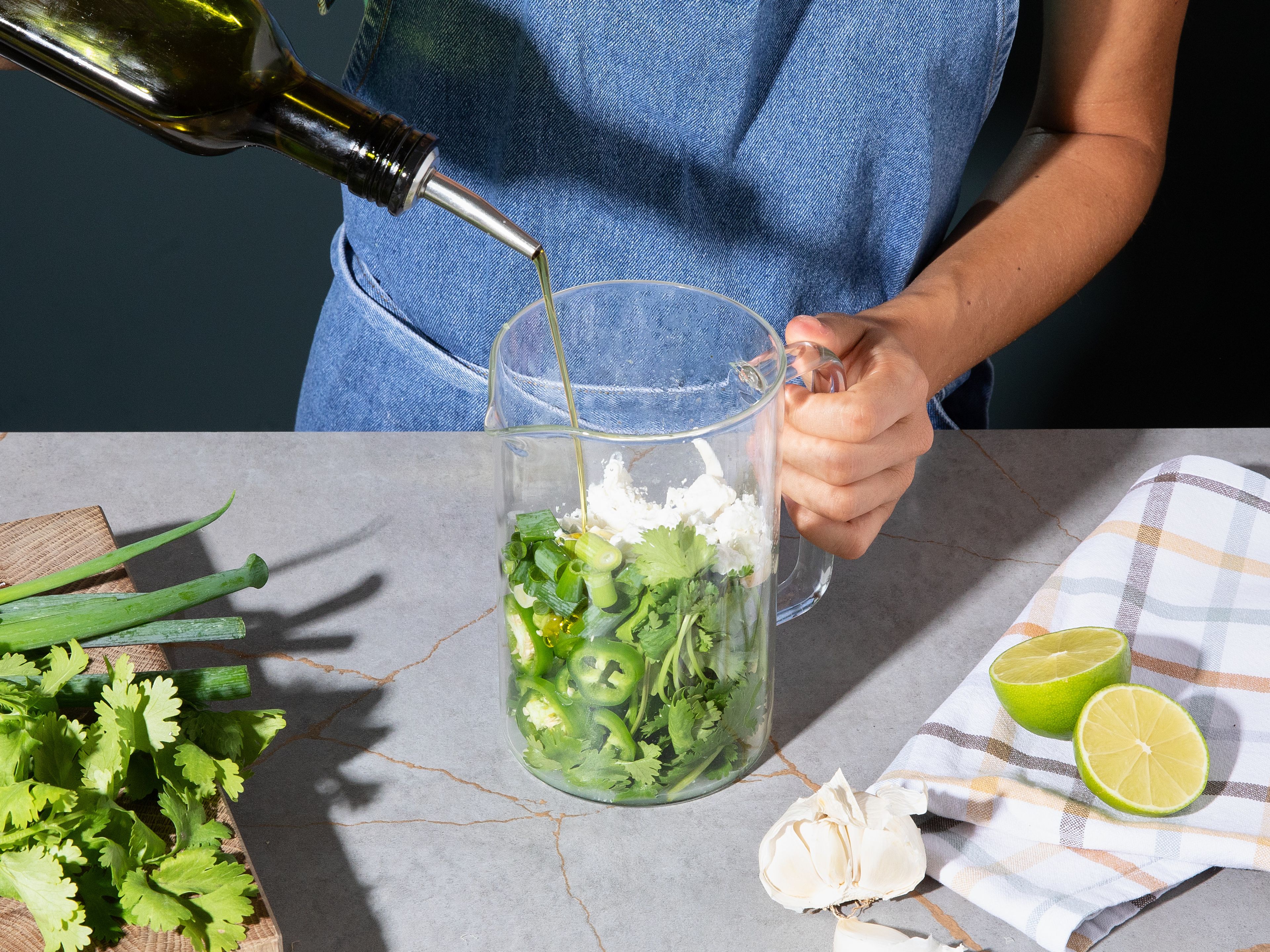 Die Hälfte der Limetten auspressen, Feta in grobe Stücke zerteilen und Knoblauch schälen. Jalapeno und Frühlingszwiebeln in grobe Stücke schneiden. Die Hälfte des Knoblauchs mit allen anderen zerkleinerten Zutaten zusammen mit dem Koriander, der Mayonnaise und Olivenöl in einen Mixer geben und zu einer glatten Soße mixen. Bei Bedarf mit Salz abschmecken.