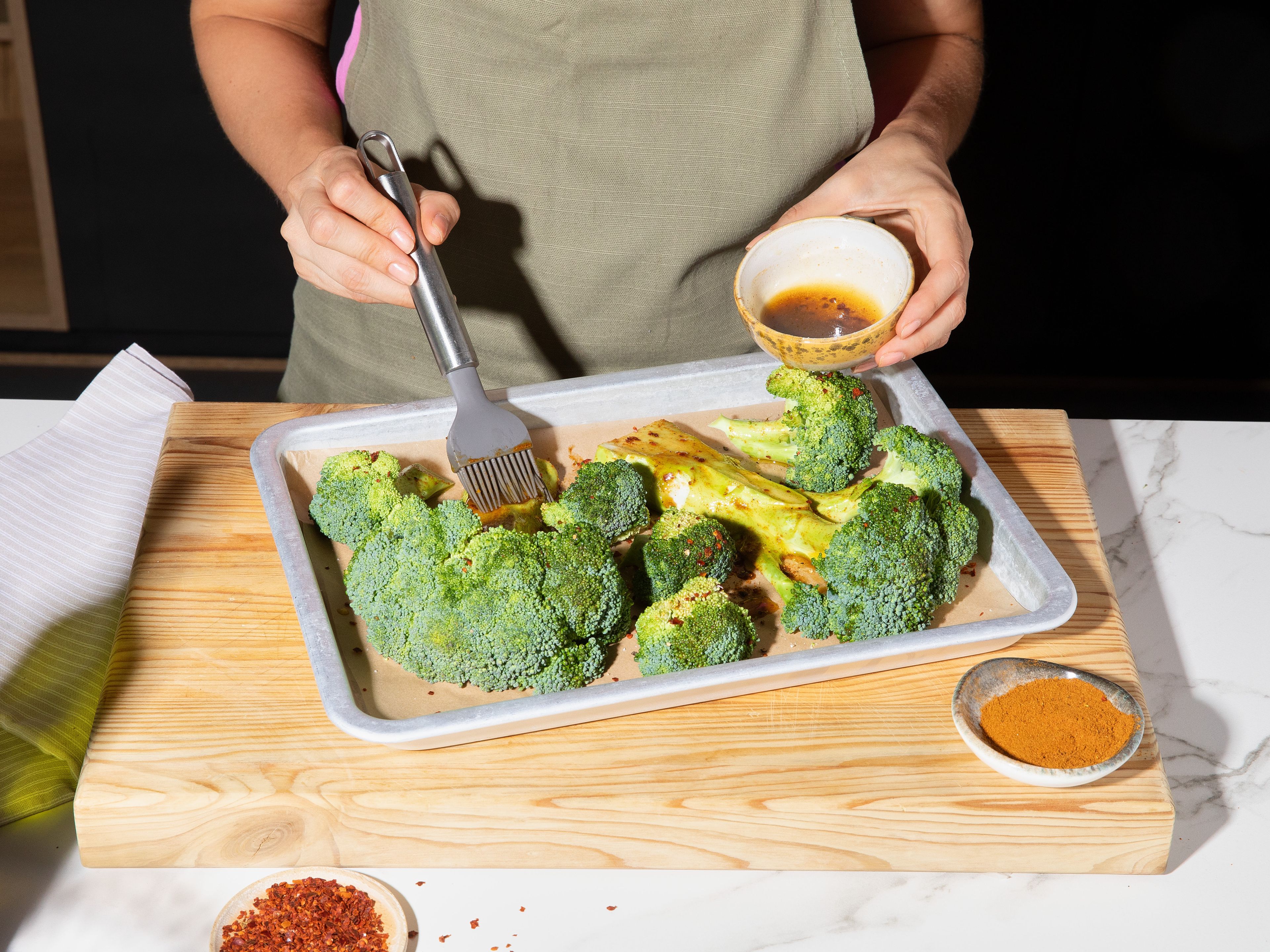 Preheat oven to 200°C/392°F. Cut broccoli lengthwise into approx. 2–3 cm/1 in. thick slices to create two steaks. Use remaining florets as well. Add to a baking sheet lined with parchment paper. Mix part of olive oil, ras el hanout, chili flakes, salt, and pepper in small bowl. Brush broccoli with the mixture on both sides. Roast in preheated oven for approx. 20 min., until broccoli is light golden brown but not too dark.