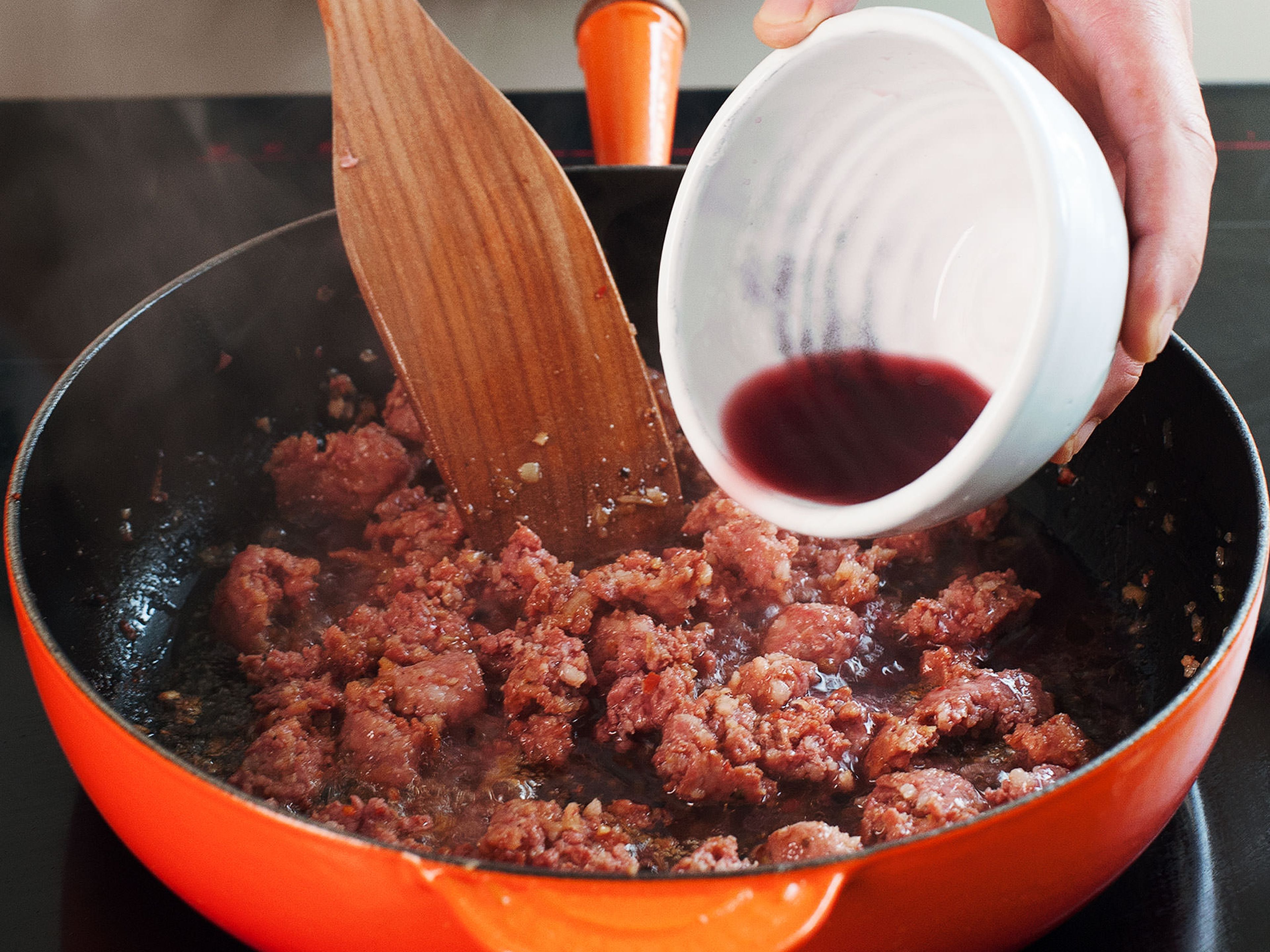 Mit Rotwein ablöschen und mit dem Kochlöffel die Röststoffe vom Pfannenboden lösen. Nach weiteren 2 - 3 Min. passierte Tomaten hinzugeben und mit Salz und Pfeffer würzen. Für weitere 5 - 10 Min. kochen lassen.