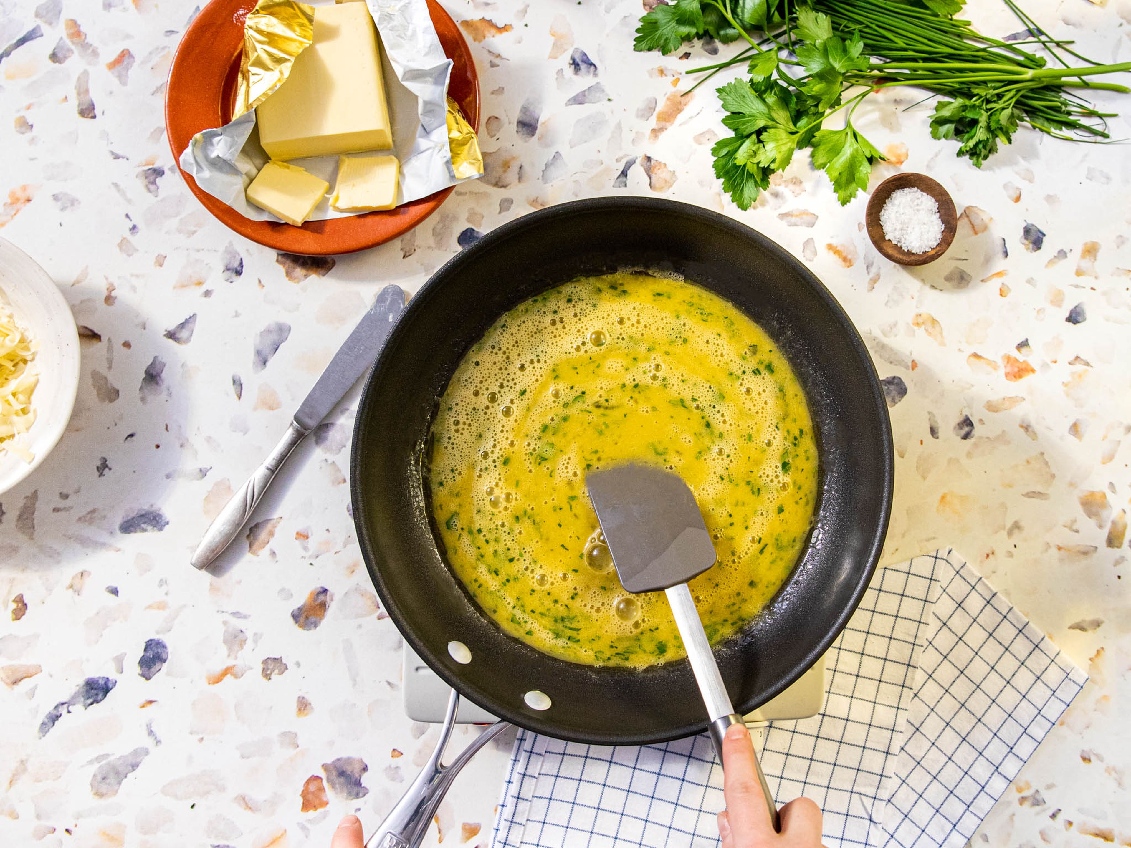 Butter in einer beschichteten Pfanne bei mittlerer bis niedriger Hitze schmelzen lassen. Eier und die Hälfte der Kräuter hinzufügen. Die Eier mit einem Pfannenwender oder mit Stäbchen verrühren und am Rand der Pfanne entlanglaufen lassen, damit sie gleichmäßig garen. Mit dem Rühren aufhören, wenn es langsam fest wird, die Mischung aber noch flüssig genug ist, um eine feste Basis zu bilden.